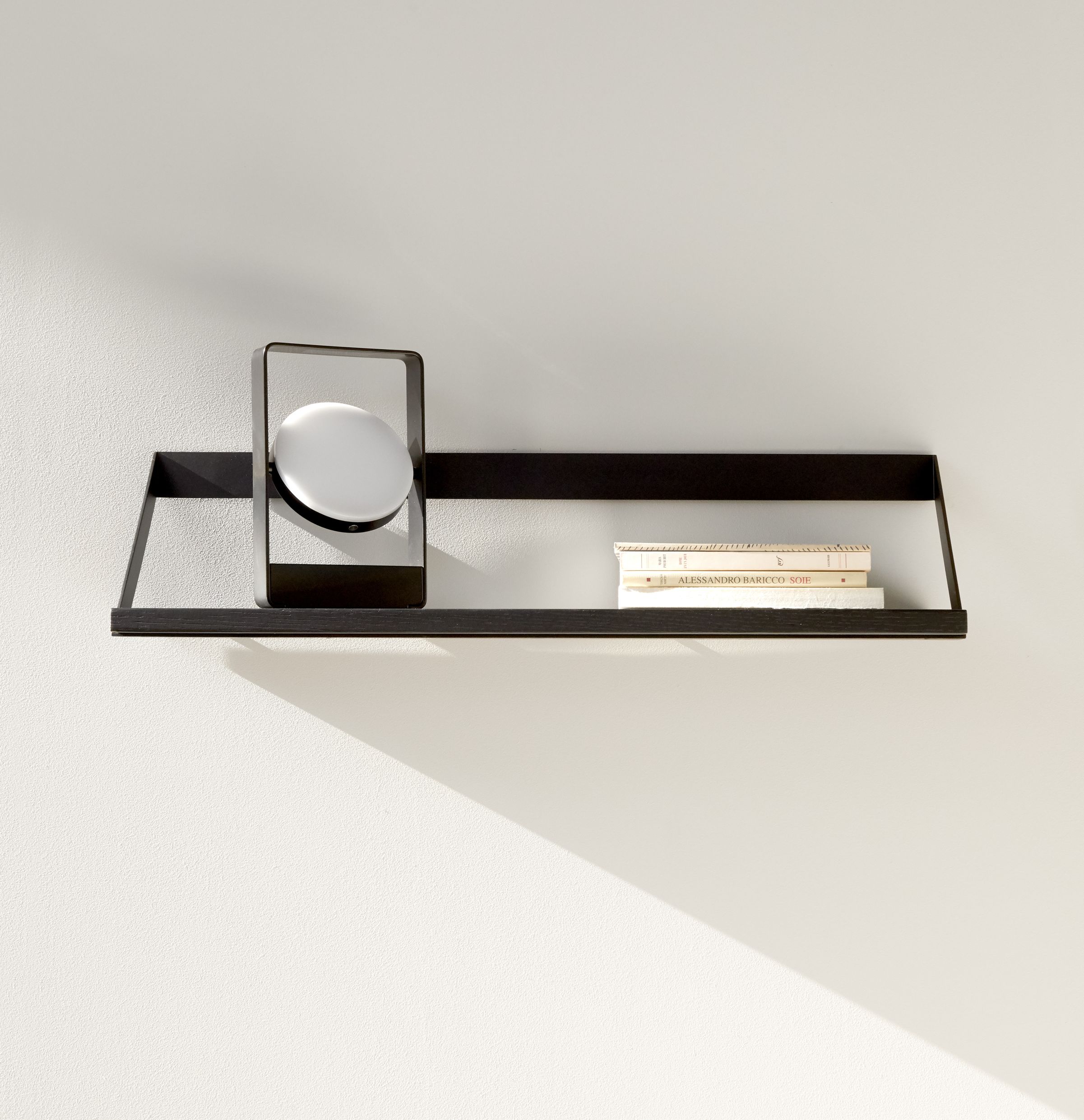 Ethnicraft Ribbon Regal aus schwarzem Eichenholz mit Lampe und Büchern an weißer Wand.