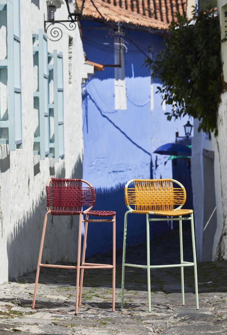Zwei Cielo Barstools Outdoor Barhocker in Rot und Gelb vor blau-weißer Hauswand.