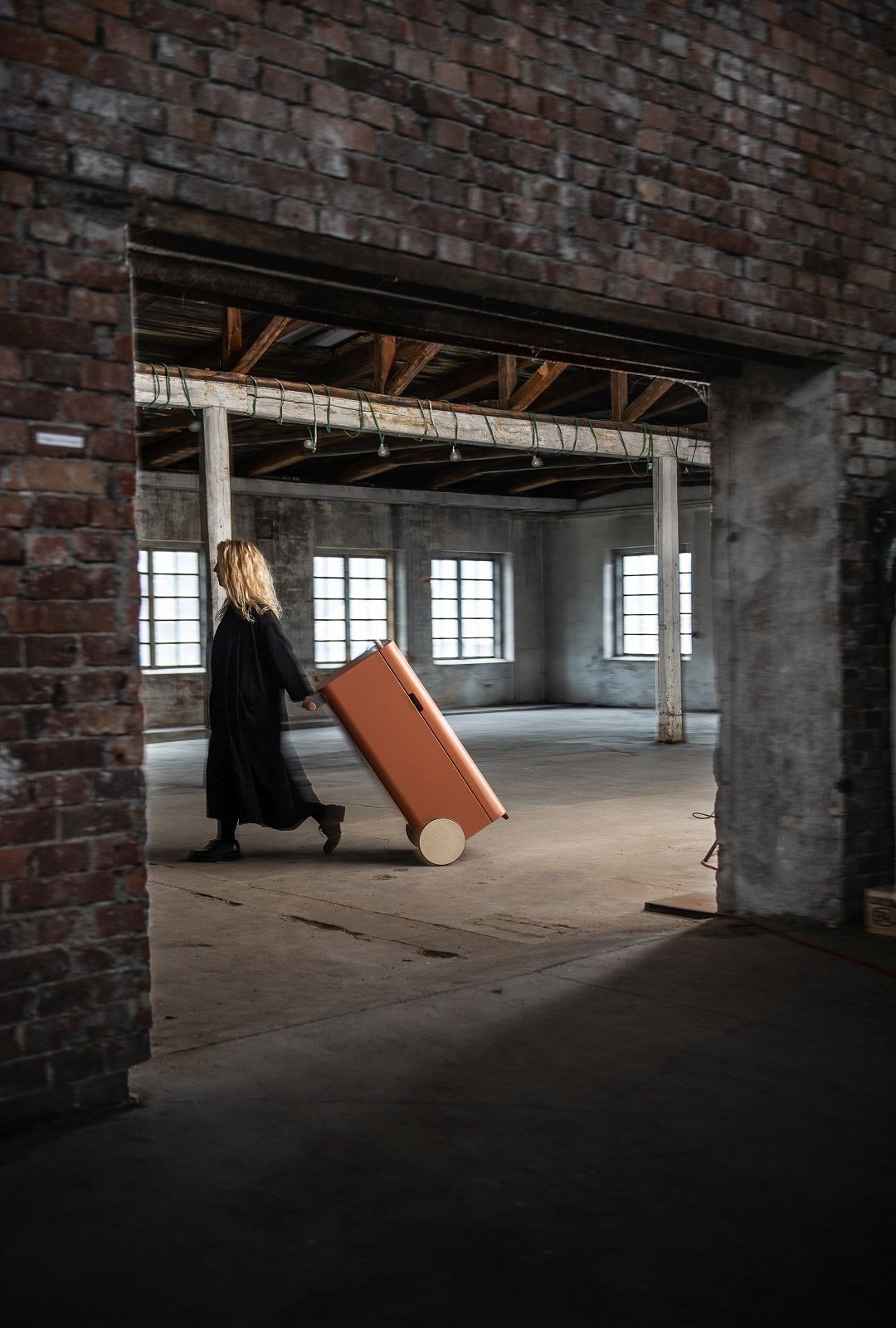 Frau zieht orangefarbenen Arkityp Mülleimer/Mülltrennung mit Rollen durch einen Raum.