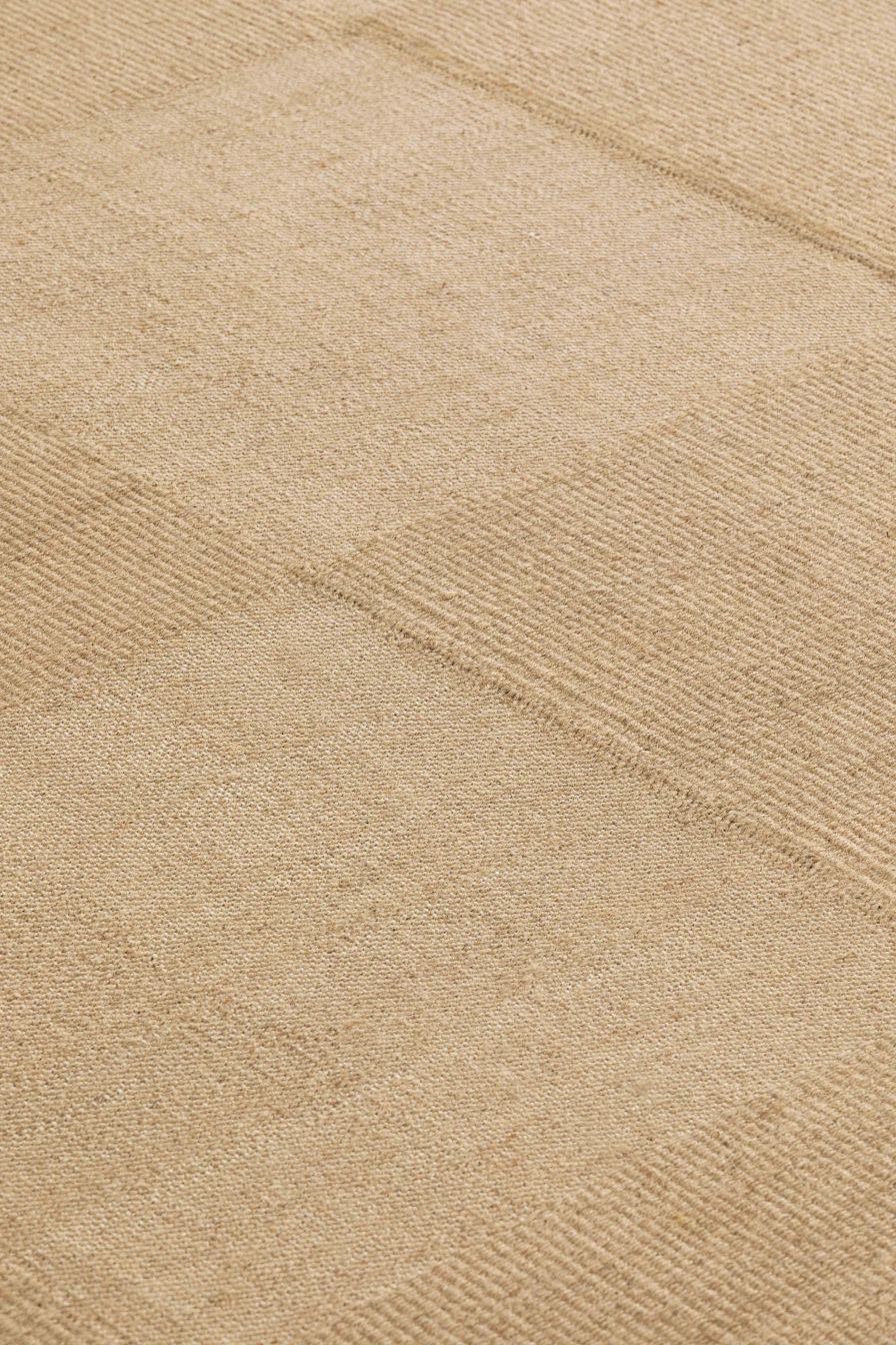 Detailaufnahme des beigen Roots Teppichs mit feiner Textur und subtilem Muster. Hochwertiger Wollteppich für Wohnräume.