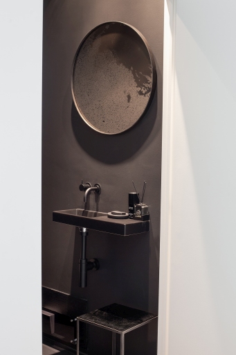 Runder Wandspiegel "heavy aged bronze" von Ethnicraft über einem dunklen Waschbecken in einem modernen Badezimmer.