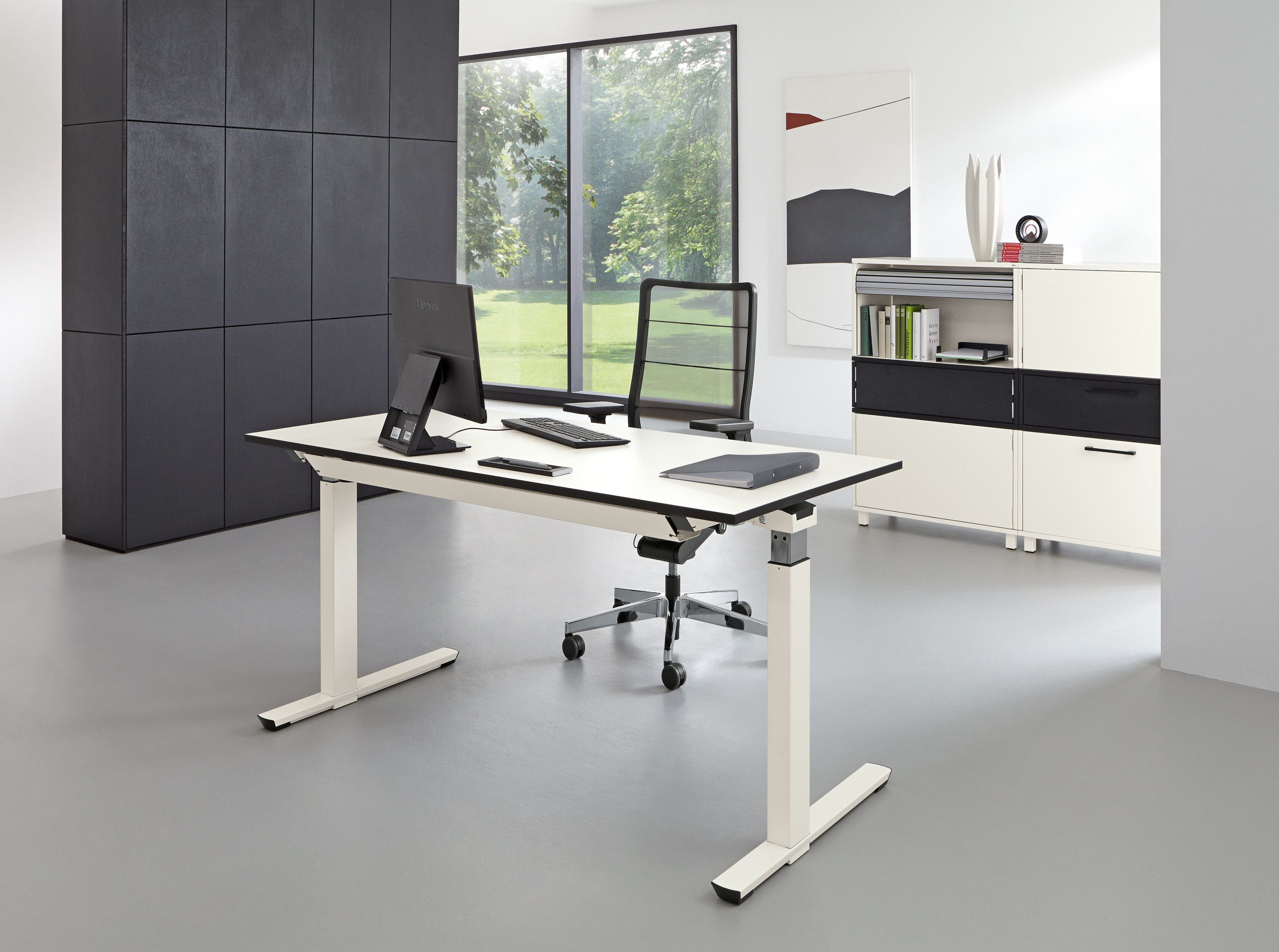 Moderner, höhenverstellbarer Palmberg Schreibtisch mit Bürostuhl, Monitor und Büromaterial in einem hellen Büro.