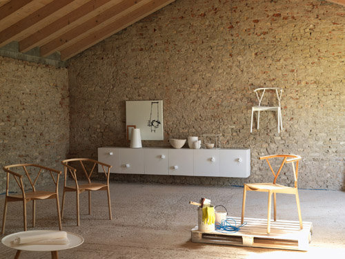 Innenaufnahme mit zwei hellbraunen Valerie Armlehnstühlen von Miniforms vor einer Wand aus Natursteinen.