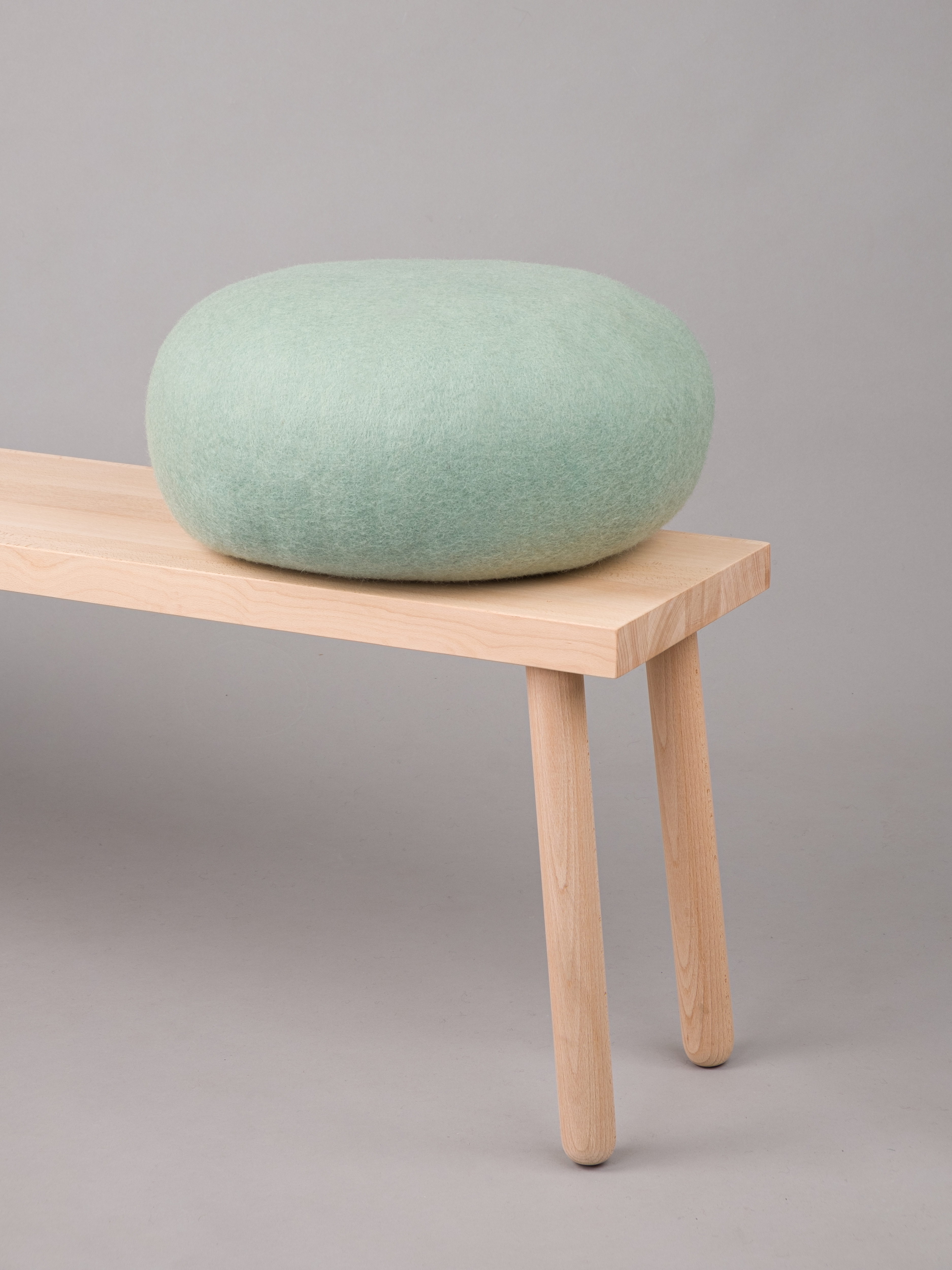 Hellgrüner Filz Pouf Hocker von myfelt auf einer hellen Holzbank. Dekorative Sitzgelegenheit.