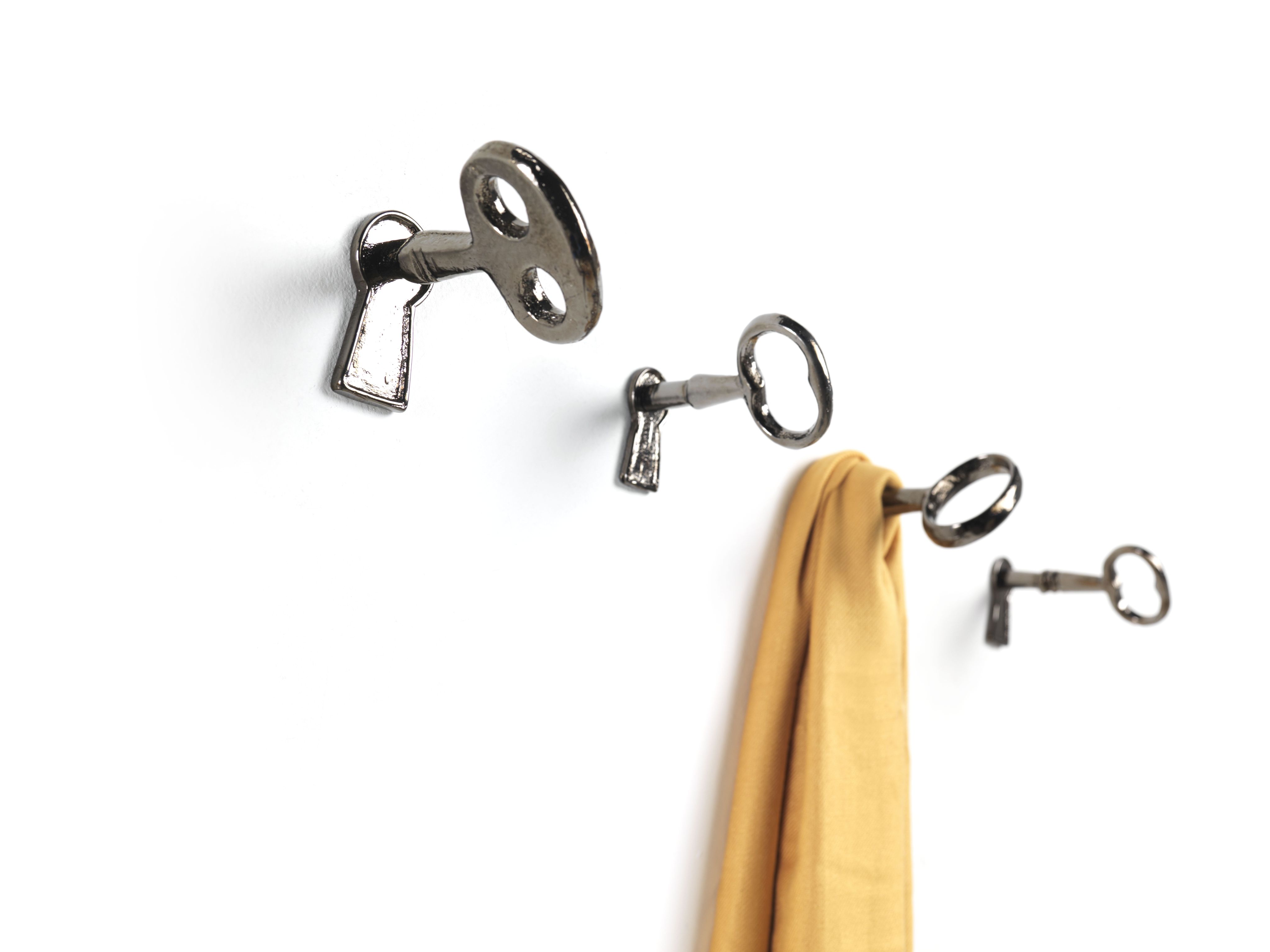 Memorie Wandhaken von Mogg: Drei silberne Schlüssel als Garderobenhaken an weißer Wand, einer mit Schal.