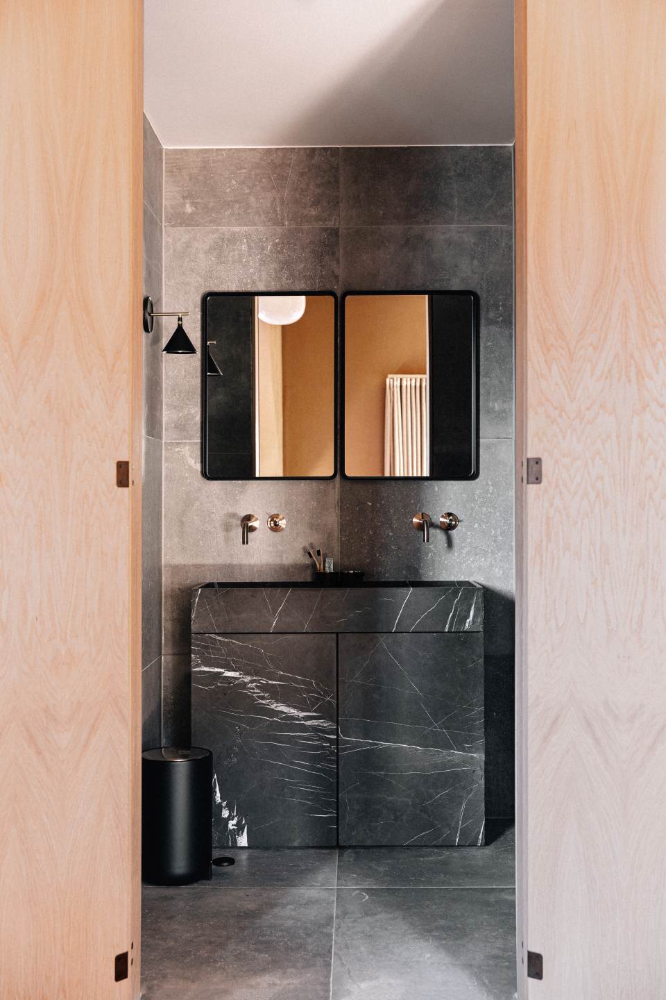 Badezimmer mit Norm Wandspiegel von Audo, rechteckig mit schwarzem Rahmen über Marmorwaschtisch.