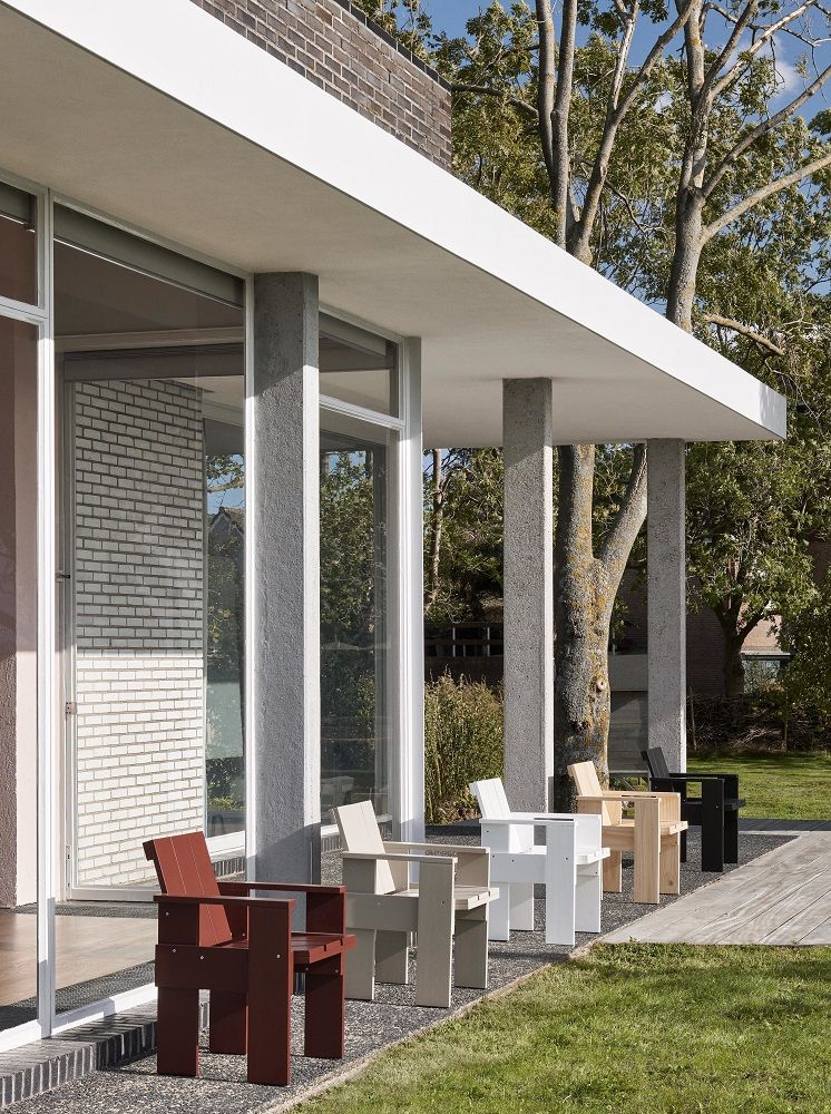 Mehrere Hay Crate Outdoor Stühle in verschiedenen Farben vor einem modernen Haus mit Garten.