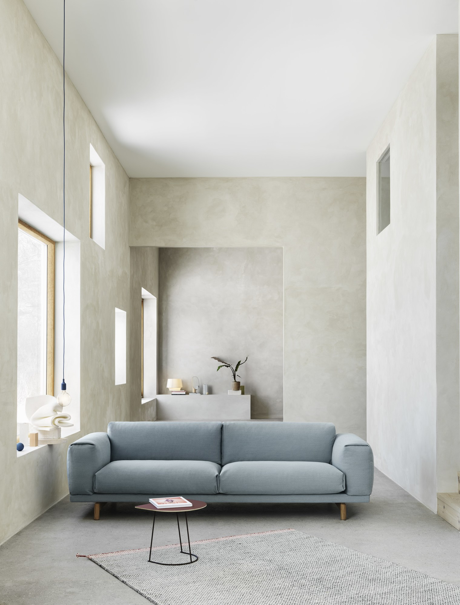 Helles Wohnzimmer mit blauem Rest Sofa von Muuto, kleinem Tisch und Teppich.