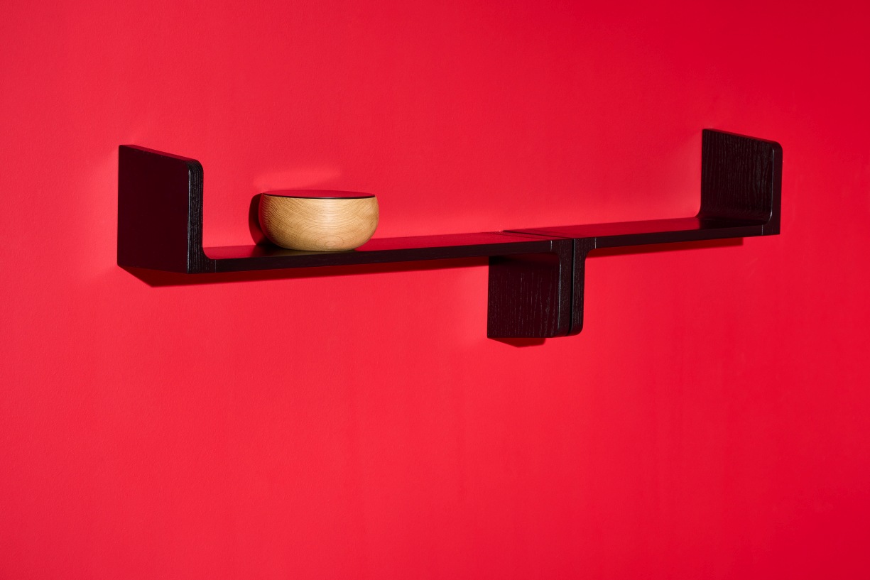 Schwarzes Ulna Wandregal von Schönbuch an roter Wand mit dekorativer Holzschale.