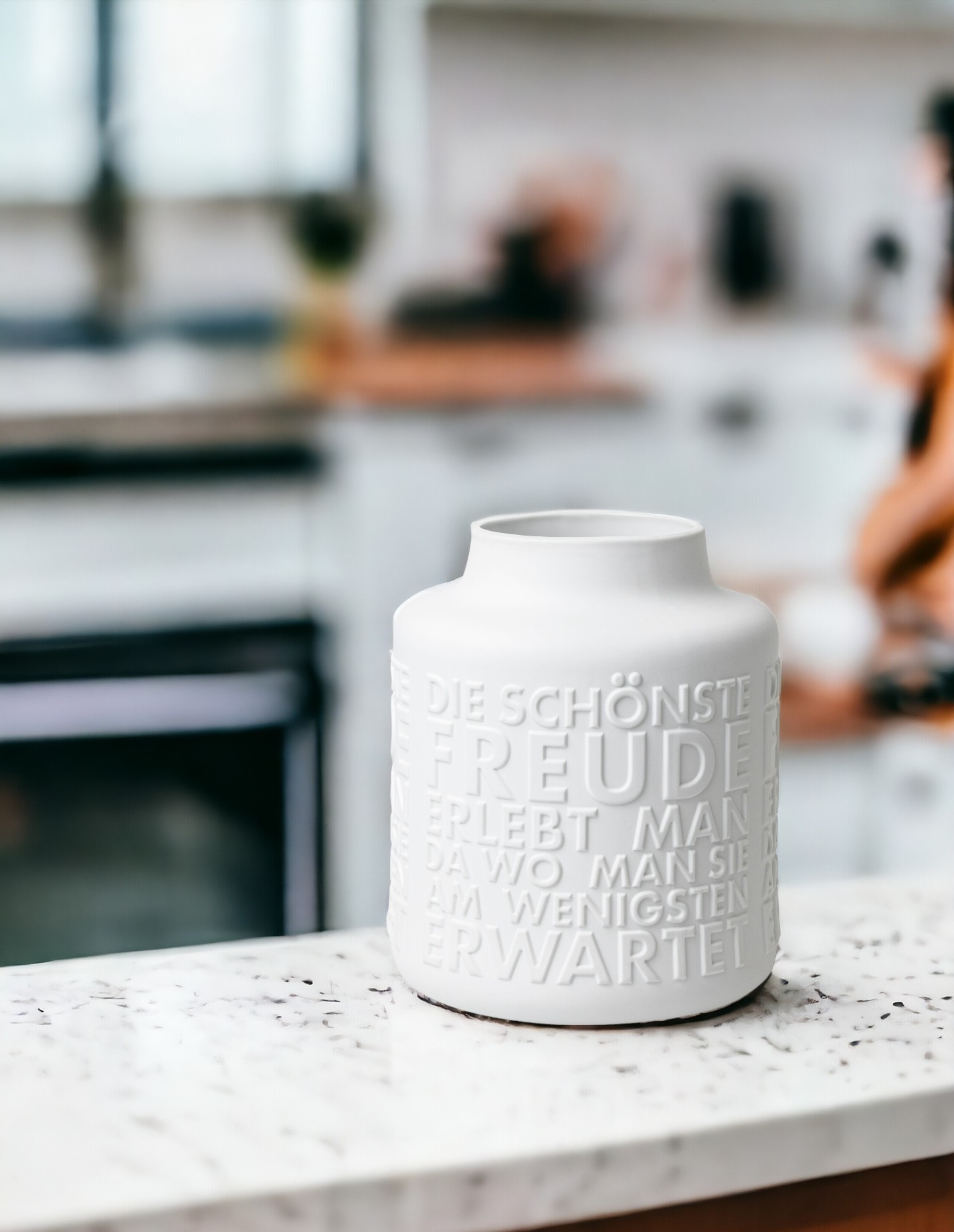 Weiße "Freude" Vase von Räder, mit erhabenem Schriftzug, dekorativ auf einer Küchenarbeitsplatte platziert.