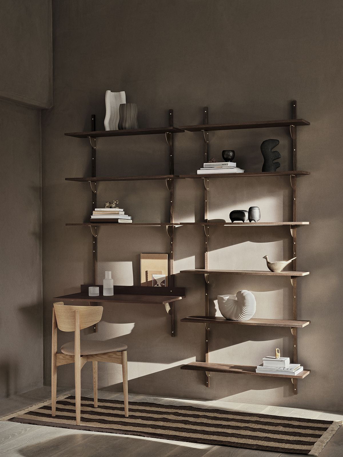 Sector Shelf Wandregal von Ferm Living in dunklem Holz mit Deko-Objekten und Stuhl.