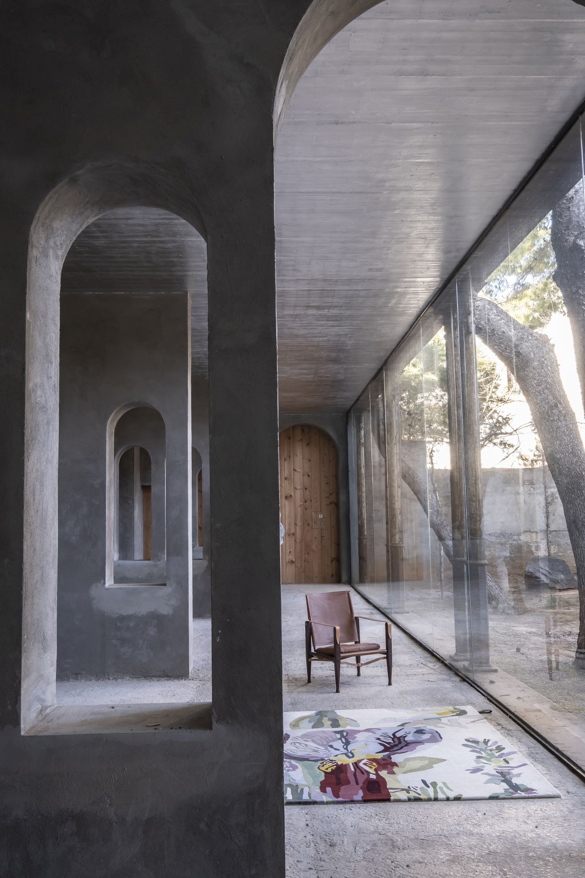 Innenaufnahme mit Nanimarquina Teppich "Flora Backyard", floralem Muster und braunem Sessel vor Fensterfront.