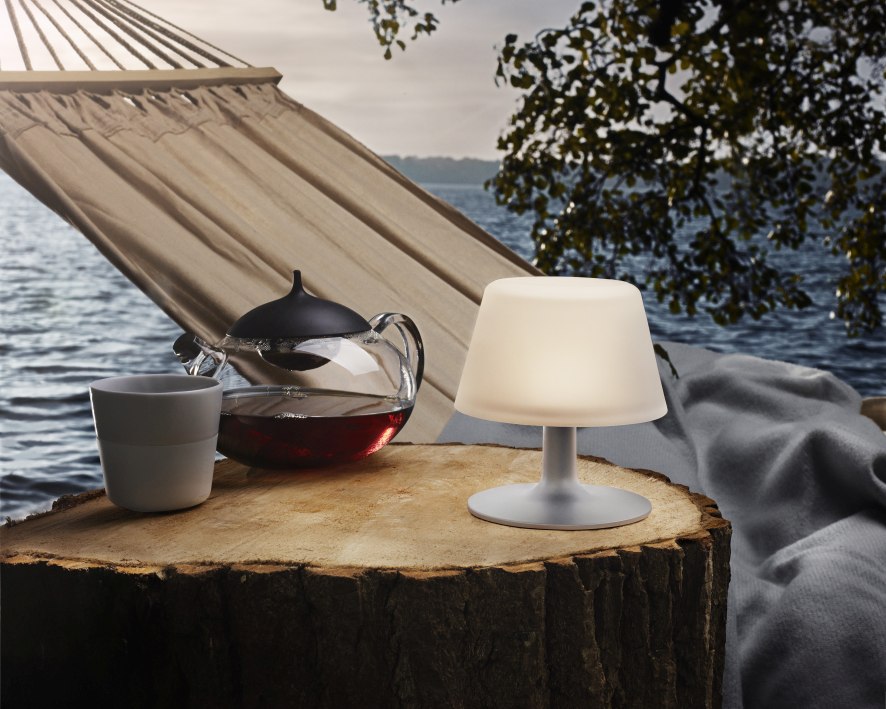 Sunlight Tischleuchte von Eva Solo auf Baumstumpf mit Tee und Hängematte im Hintergrund.