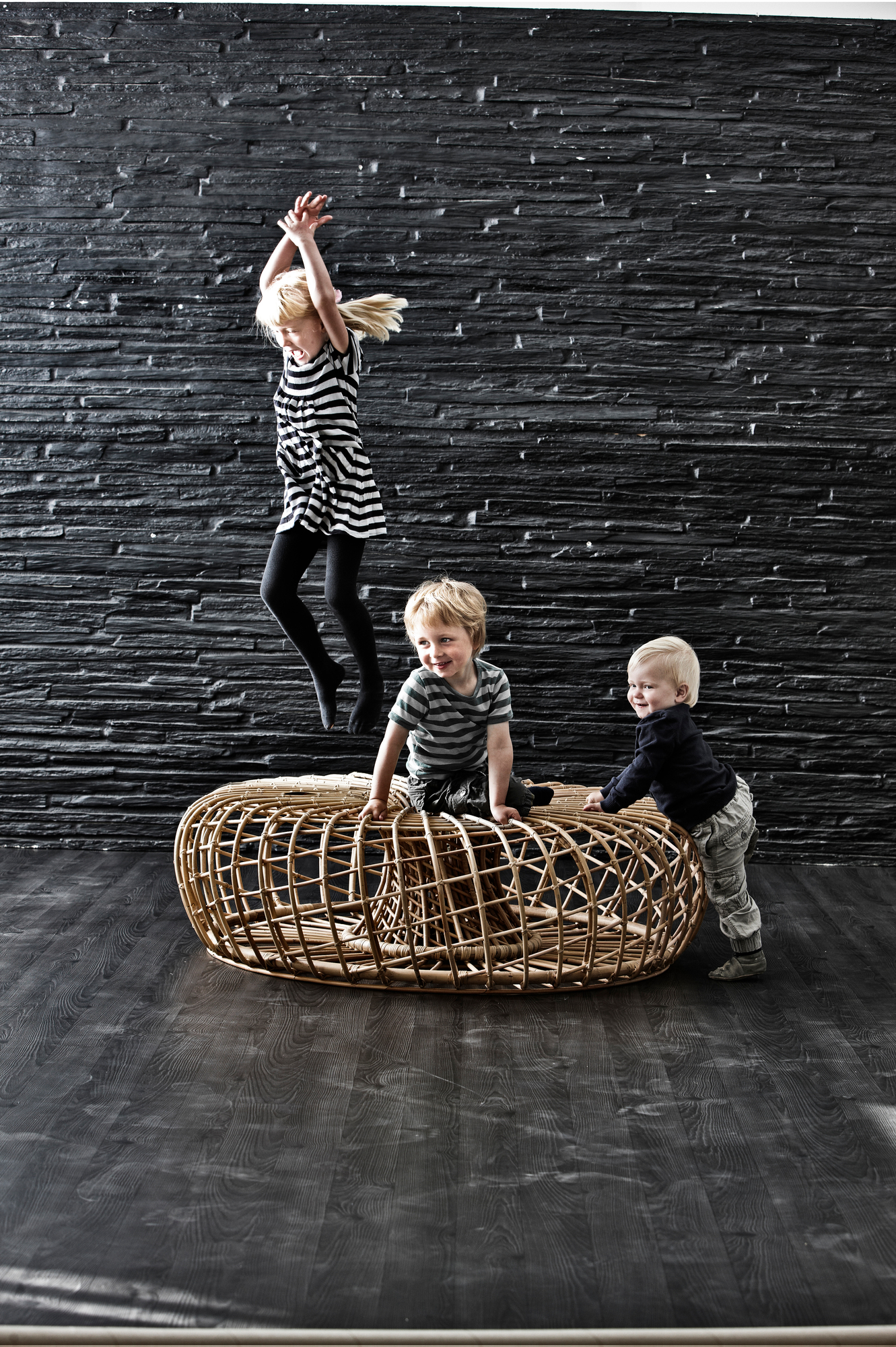 Kinder spielen mit dem Nest Indoor Hocker von Cane-Line, einem großen, geflochtenen Sitzmöbel.