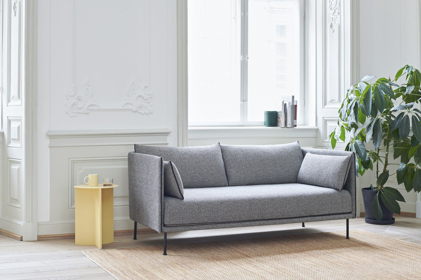 Graues Silhouette Sofa 2-Sitzer Low von Hay im hellen Wohnzimmer mit Beistelltisch und Zimmerpflanze.
