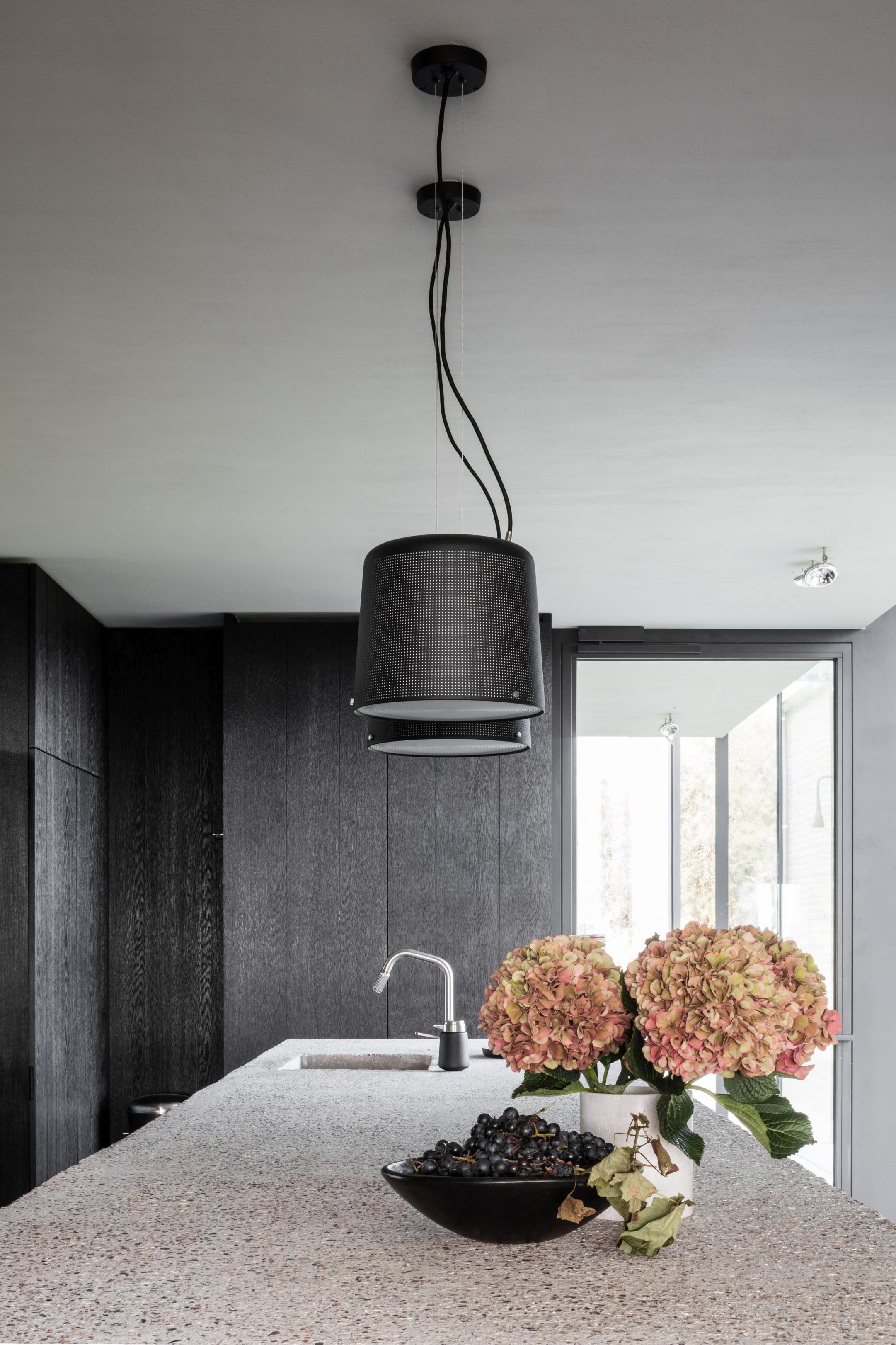 Schwarze Vipp Pendelleuchte klein über Kücheninsel mit Blumen und Obst. Design Lampe.