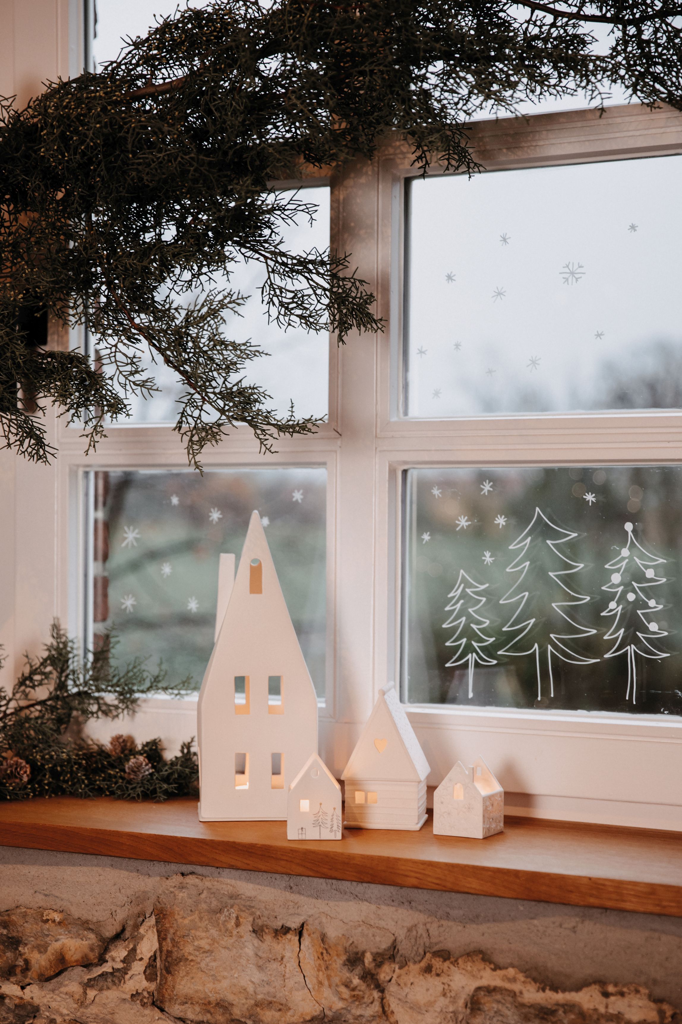 Weihnachtliche Dekoration mit Lichthaus Spitzdach, Keramik Häuser und Fensterbild mit Tannenbäumen.