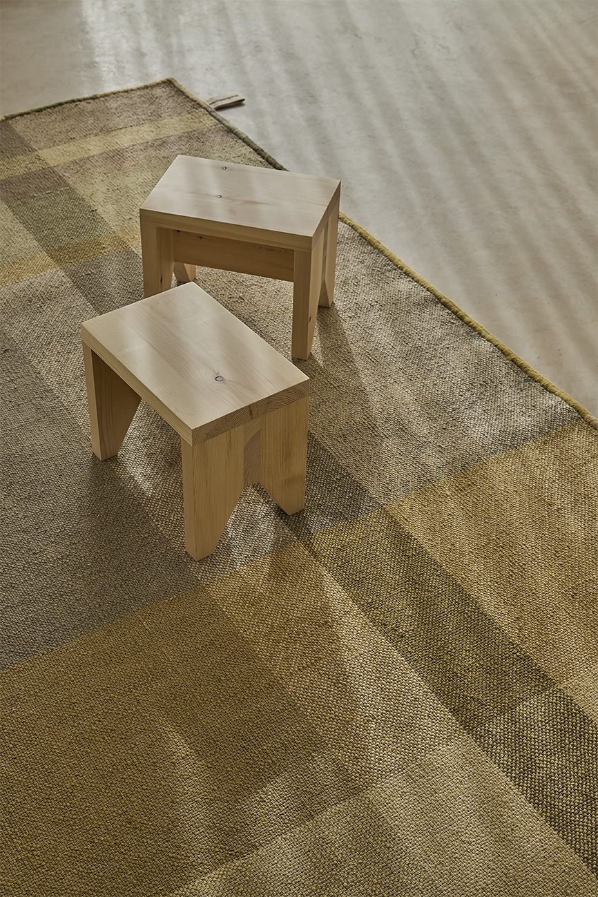Nuance Teppich Nanimarquina: Detailaufnahme des Teppichs mit geometrischem Muster in Limettönen und zwei Holzhockern.