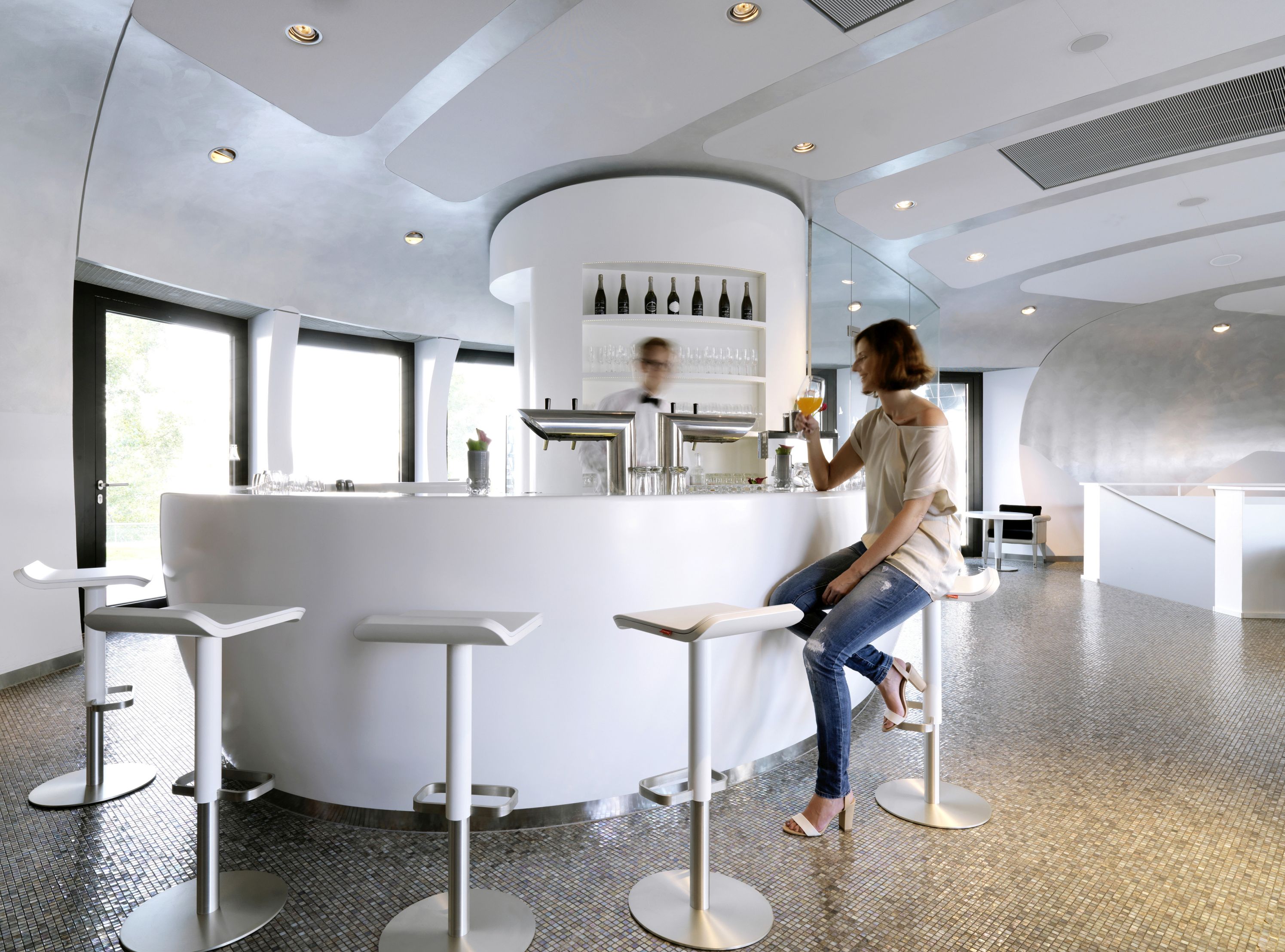 Frau sitzt auf einem weißen, höhenverstellbaren ED Barhocker von Moree an einer Bar.