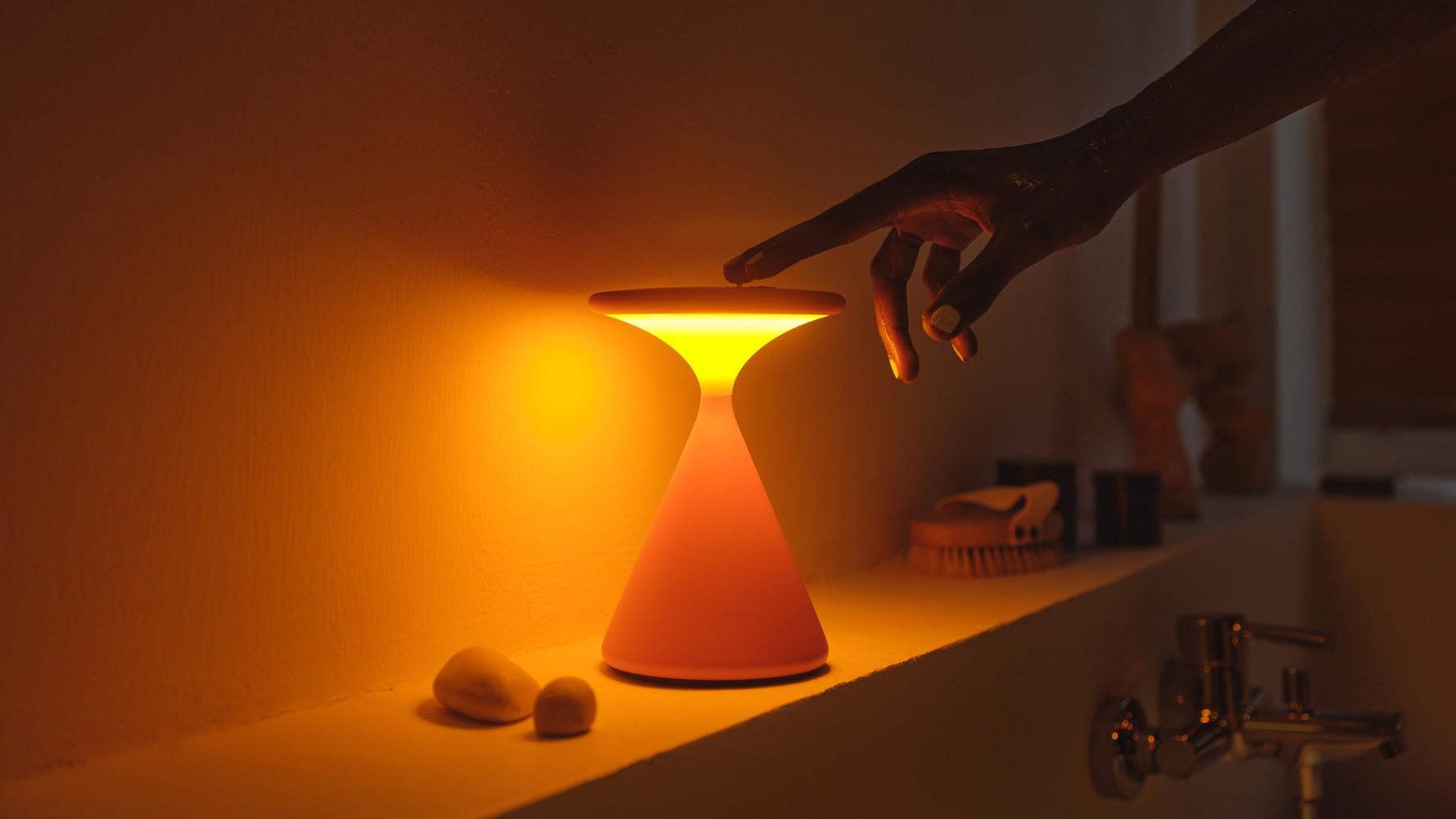 Salt Akkuleuchte in Grau-Sandweiß: Moderne Tischleuchte spendet warmes Licht, Finger berührt die Lampe.