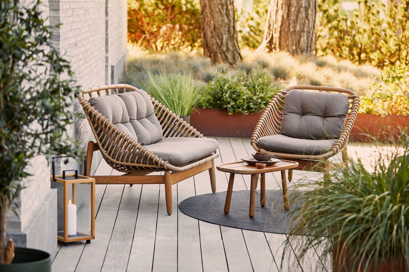 Strington Outdoor Sofa von Cane-Line: Zwei Rattansessel mit grauen Kissen und Holztisch auf Terrasse.