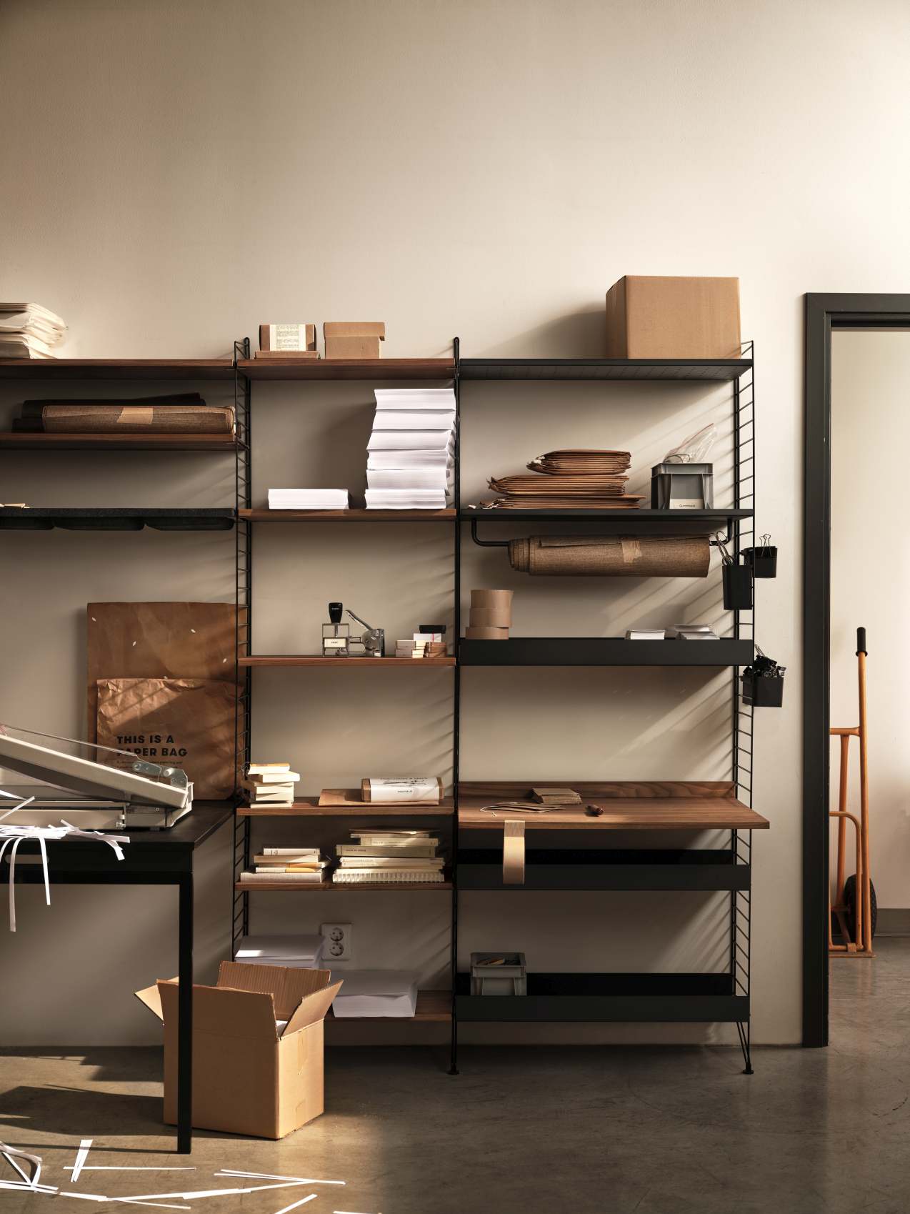 Wohnzimmer mit String Furniture Regalsystem in Schwarz und Holz, gefüllt mit Büroartikeln.