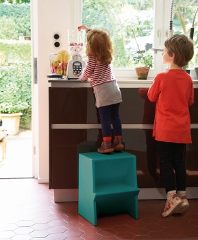 Kinder auf farbigem Tritthocker in Küche. Tritthocker als Möbel für Kinderzimmer und Küche.