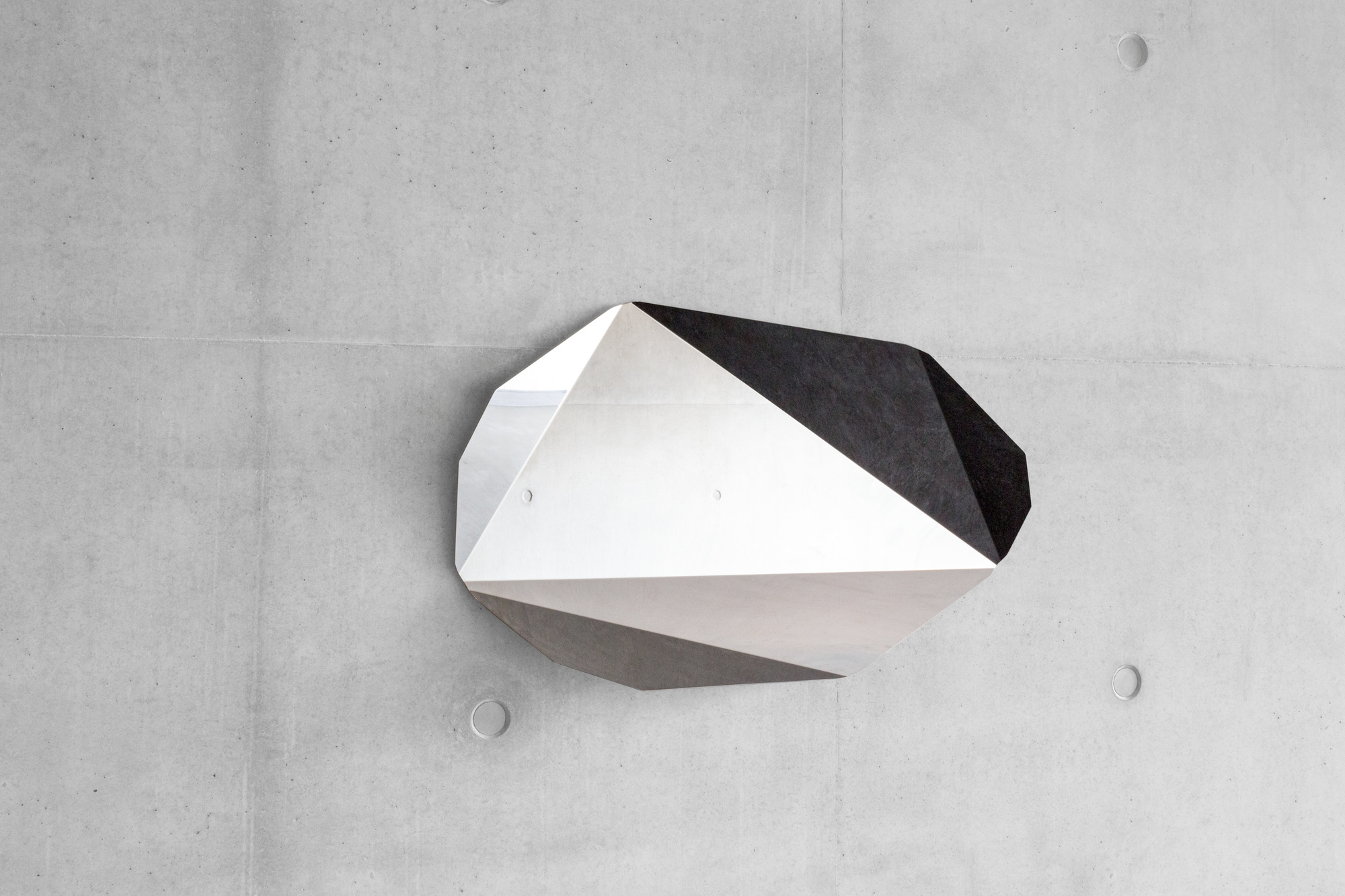 Piega Mirror Wandspiegel von ClassiCon, kleine Ausführung. Design Wandspiegel mit geometrischem Design an Betonwand.