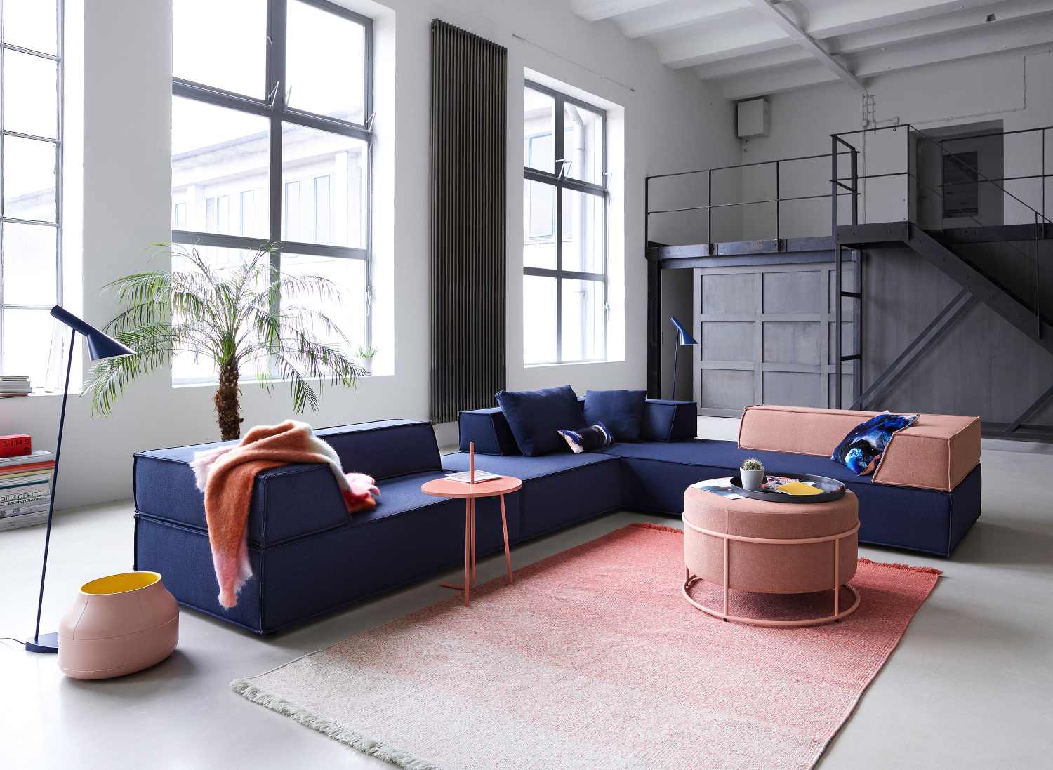 Helles Wohnzimmer mit blauem Cor Trio Sofa, rosa Teppich und Beistelltisch, modulare Sitzelemente.