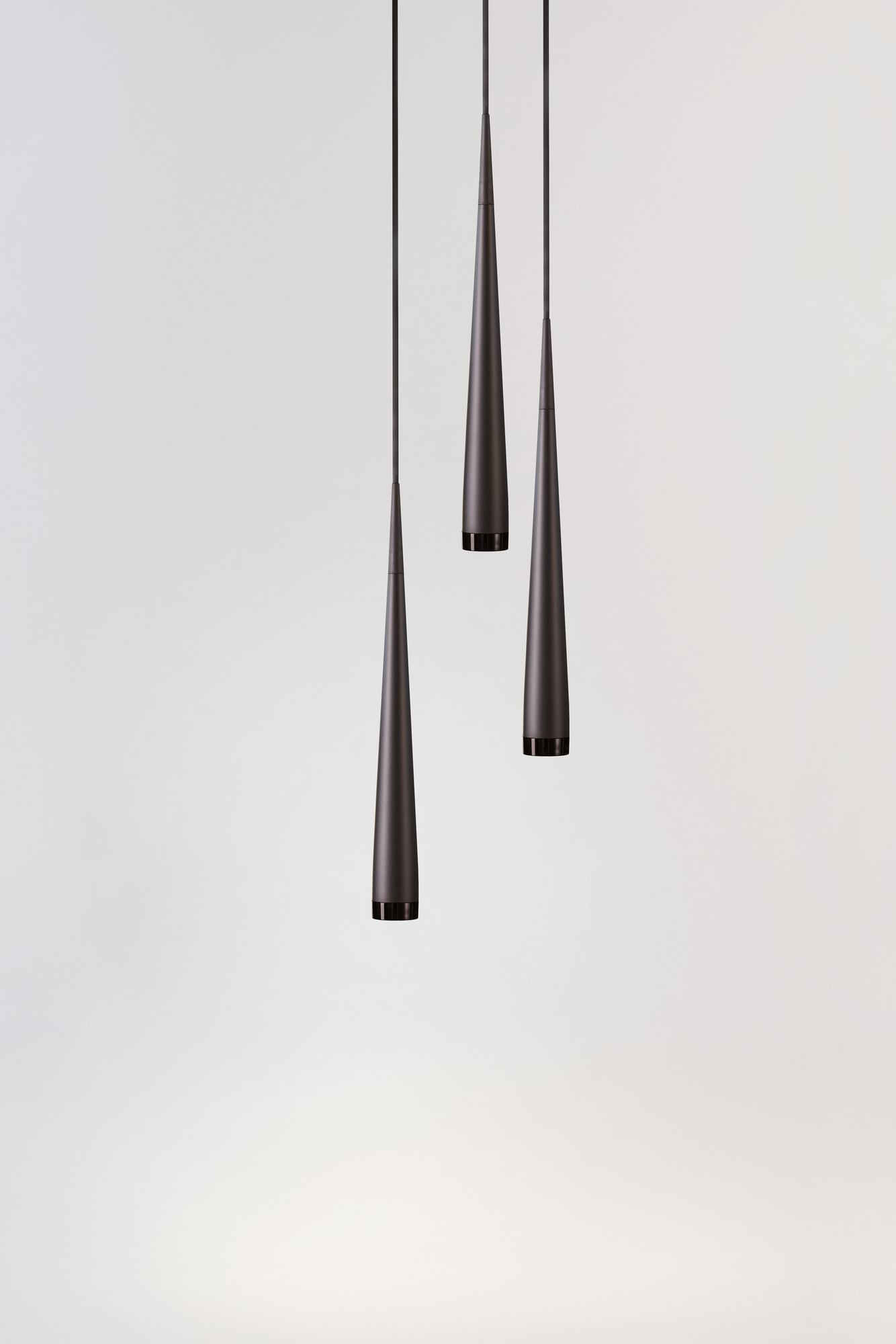 Drei graue, kegelförmige Pendelleuchten von Niceone hängen vor einem hellen Hintergrund.