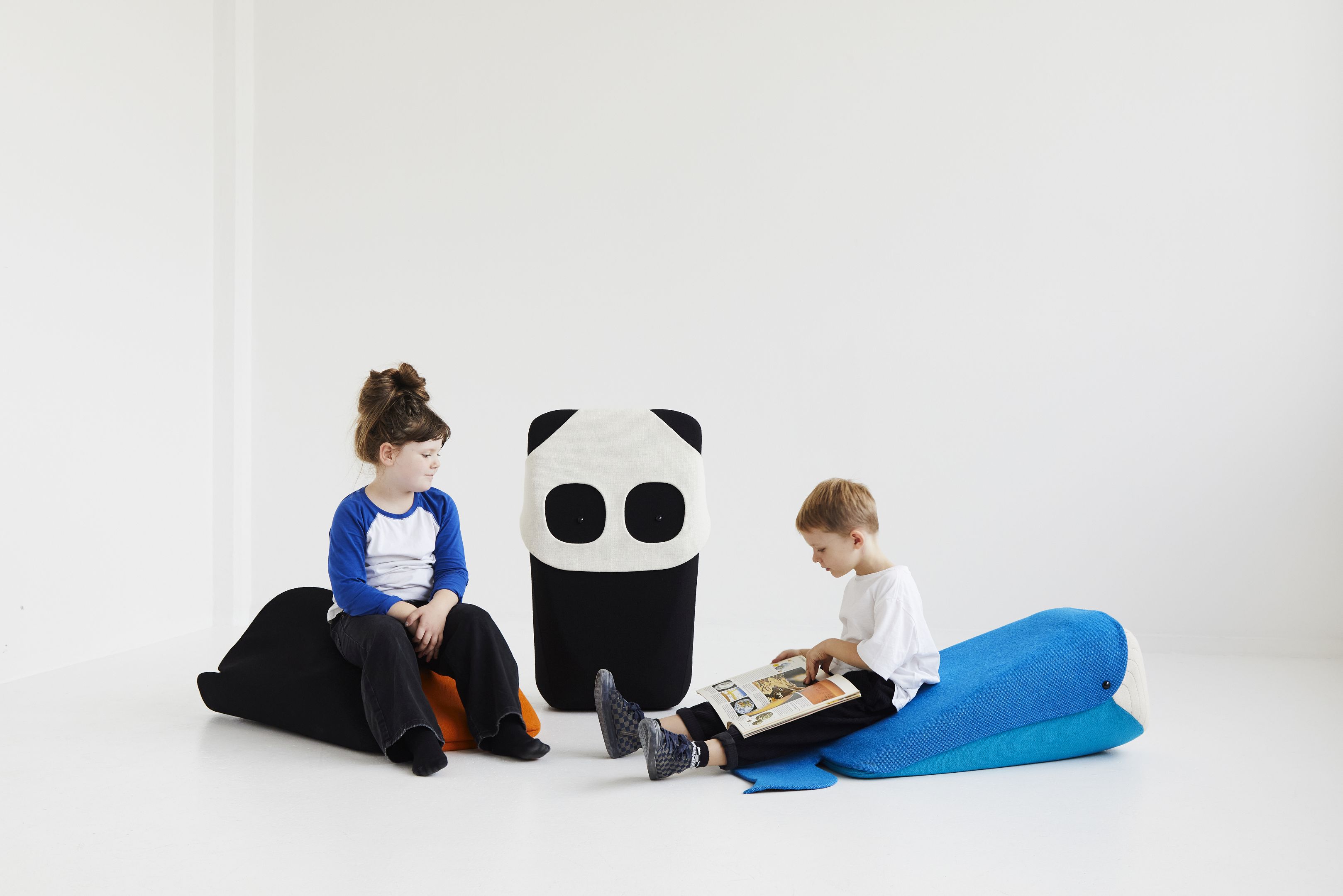 Zwei Kinder sitzen auf EO Denmark Sitzkissen: Mädchen auf schwarzem Wal, Junge auf blauem Wal.