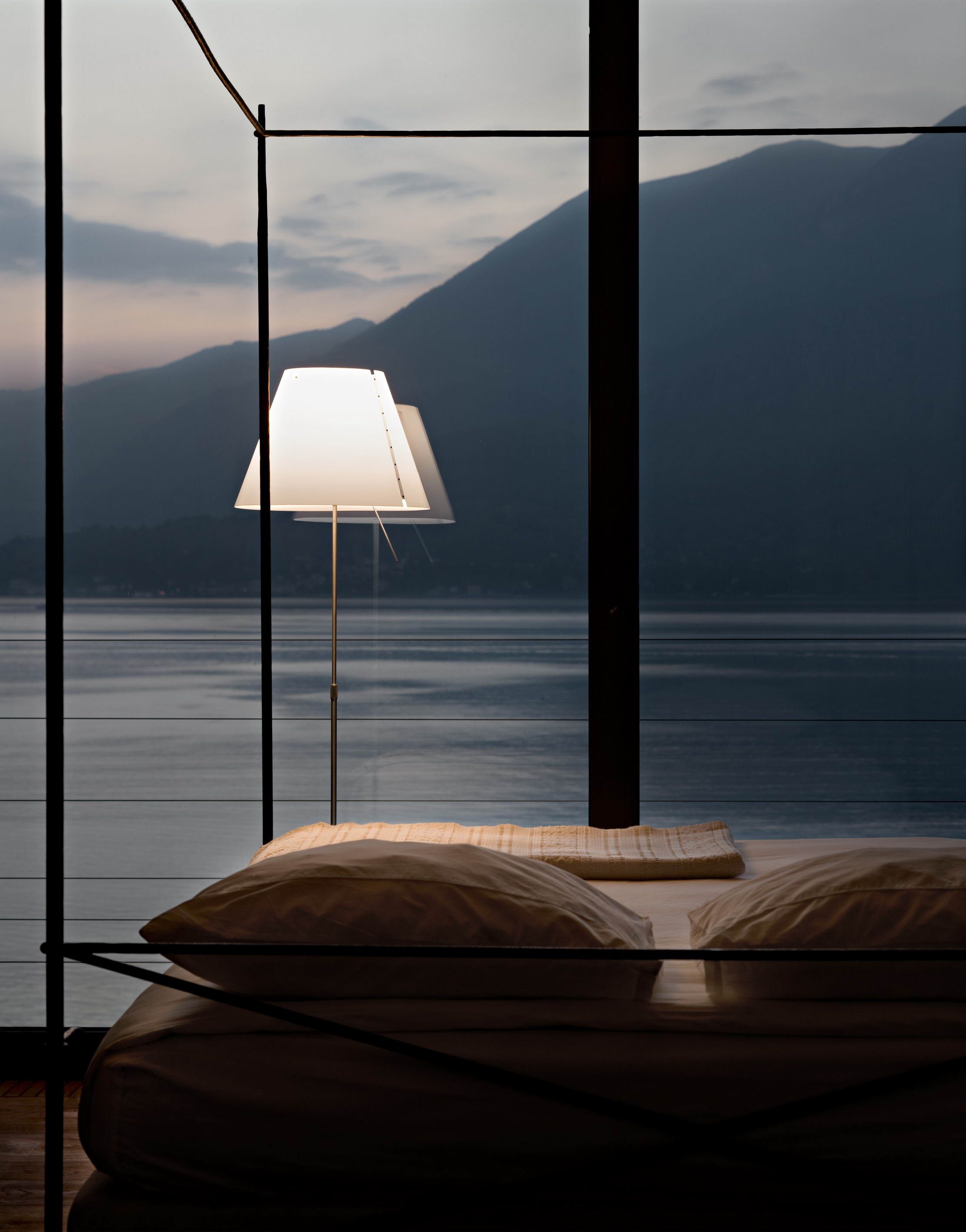 Grande Costanza Stehleuchte von Luceplan neben einem Bett mit Seeblick. Design Lampe.