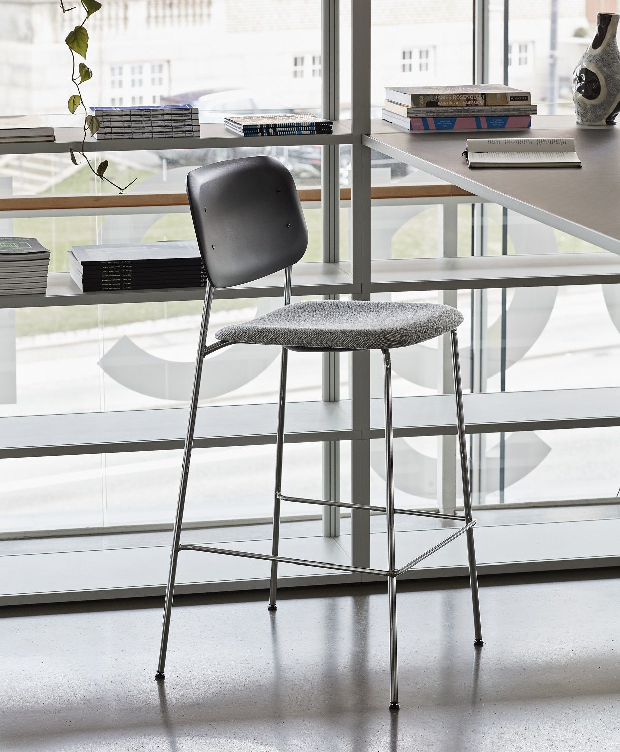 Hay Soft Edge Barhocker mit grauem Sitz und Rückenlehne, Chromgestell vor Fenster.