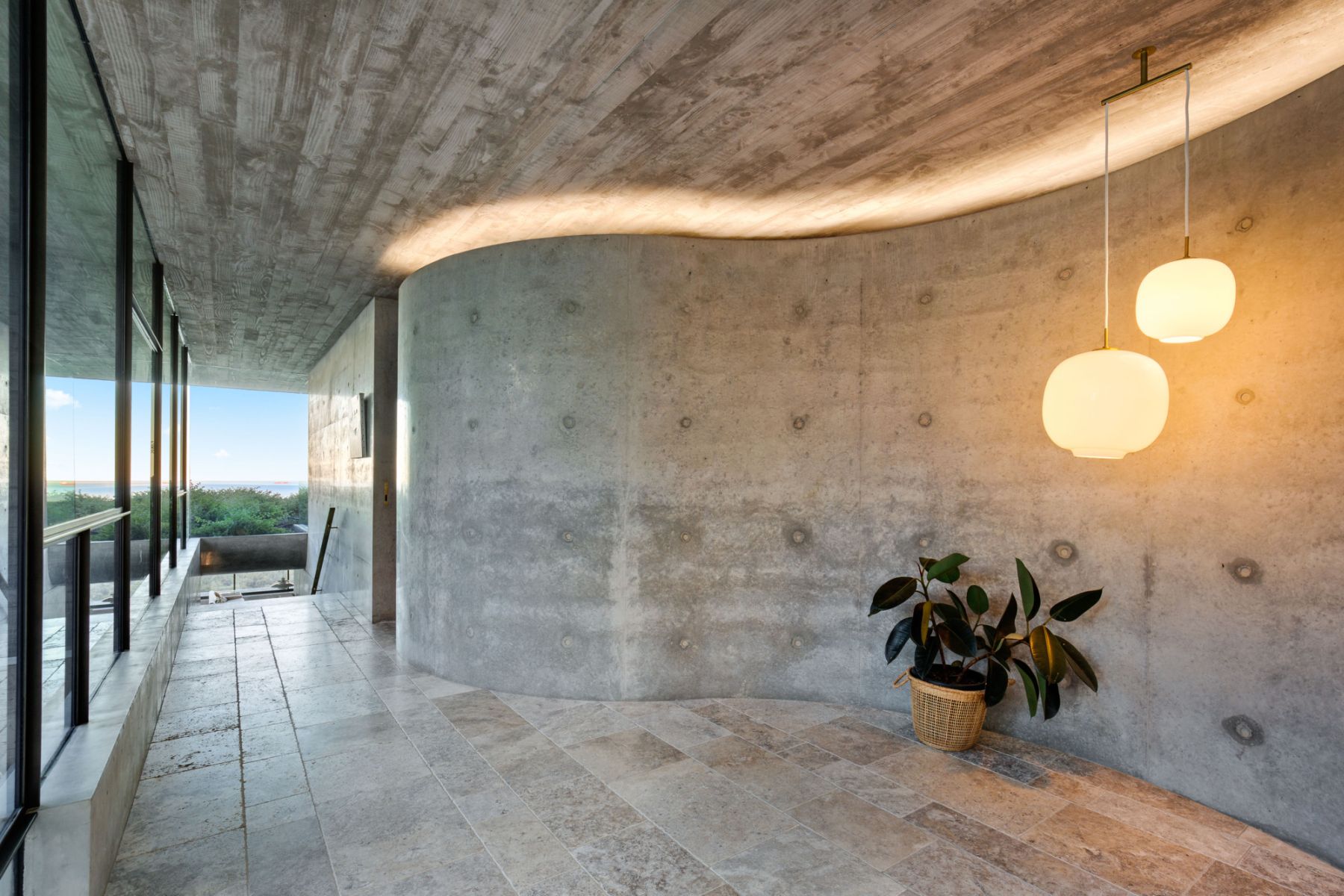 Innenaufnahme mit VL45 Radiohus Pendelleuchten von Louis Poulsen, die ein modernes Interieur mit Betonwänden und Natursteinboden beleuchten.