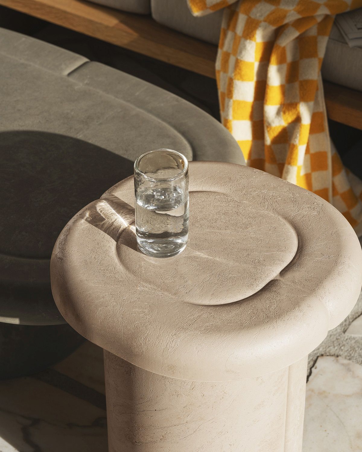 Nahaufnahme des Alder Couchtisches von Mater, oval, beige, mit Wasserglas. Indoor/Outdoor geeignet.