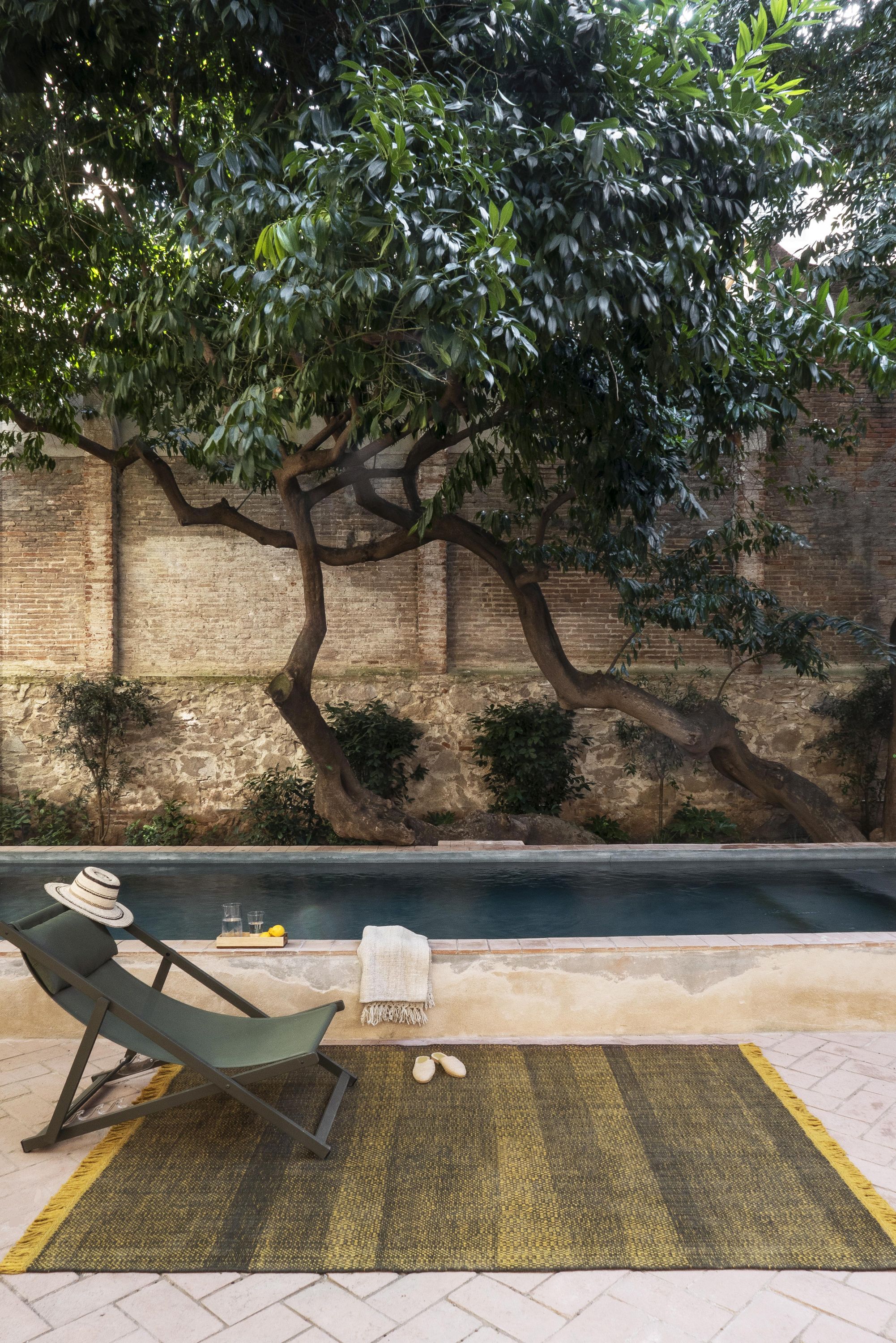 Nanimarquina Tres Outdoor Texture Teppich in Senf neben Pool und Liegestuhl im Garten.