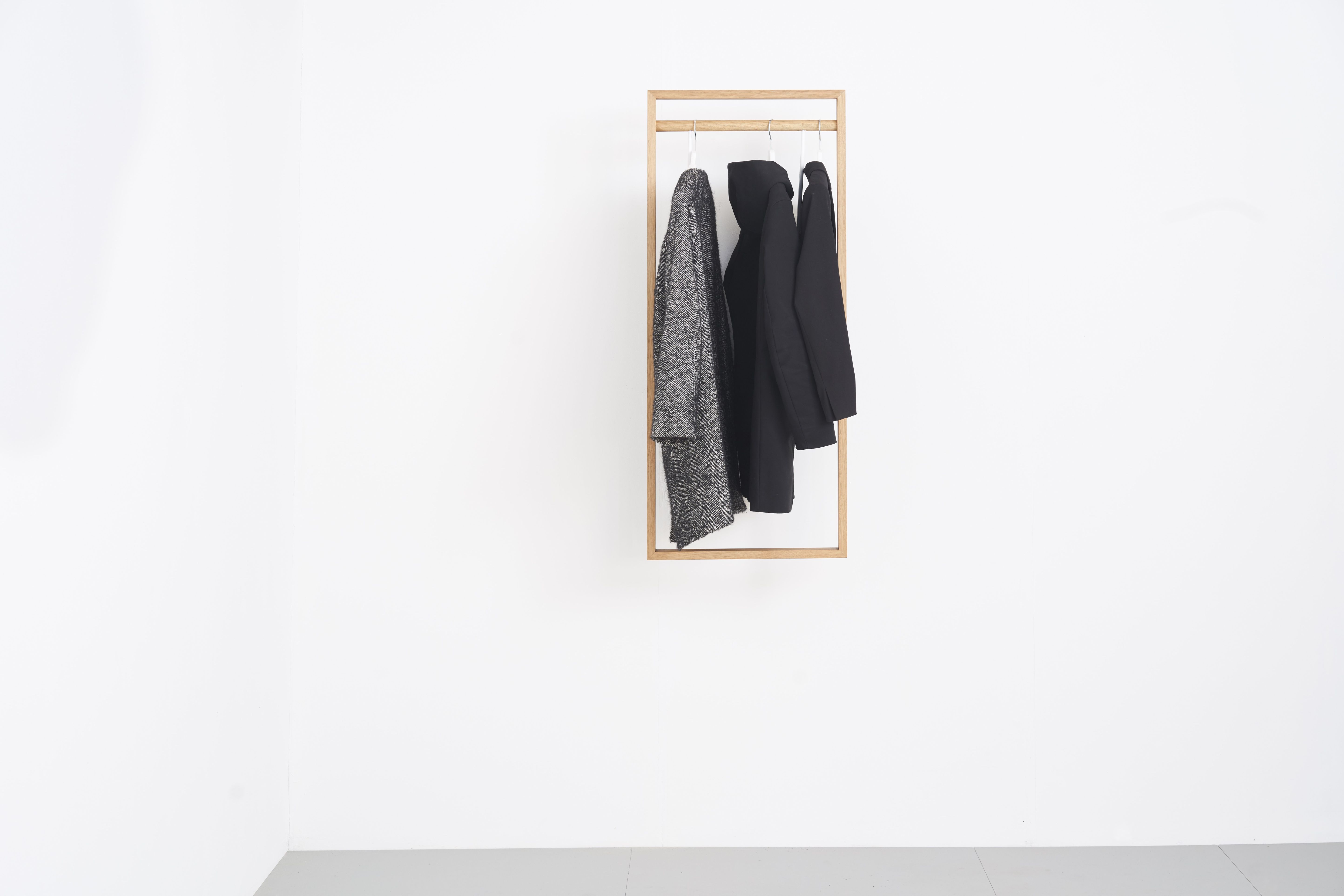 gardero-b Wandgarderobe: Helle Holzgarderobe mit zwei hängenden Jacken an einer weißen Wand.