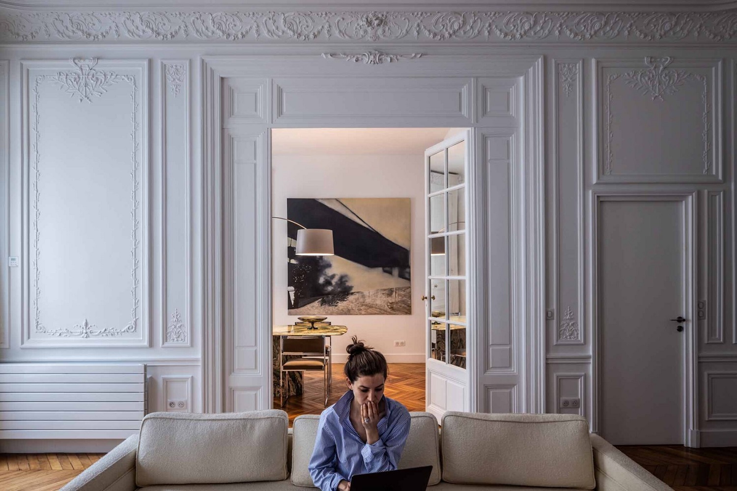 Eine Frau sitzt auf einem Sofa, im Hintergrund die Twiggy Bogenleuchte von Foscarini.