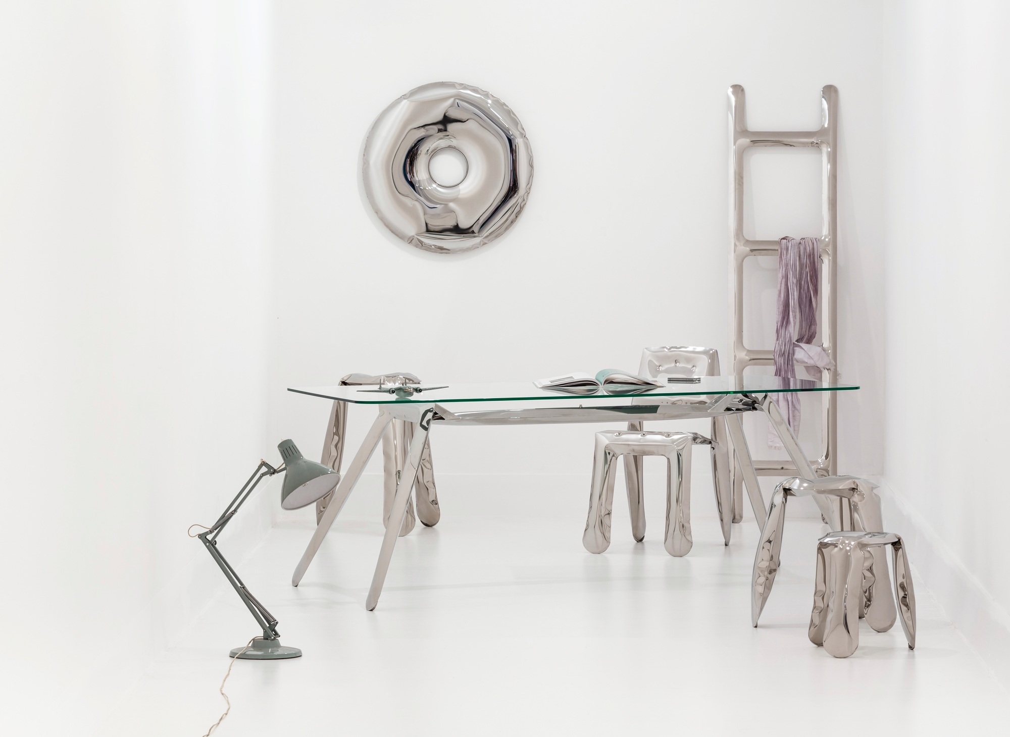 Silberner Rondo Spiegel von Zieta über einem minimalistischen Schreibtisch mit Stühlen und Lampe.