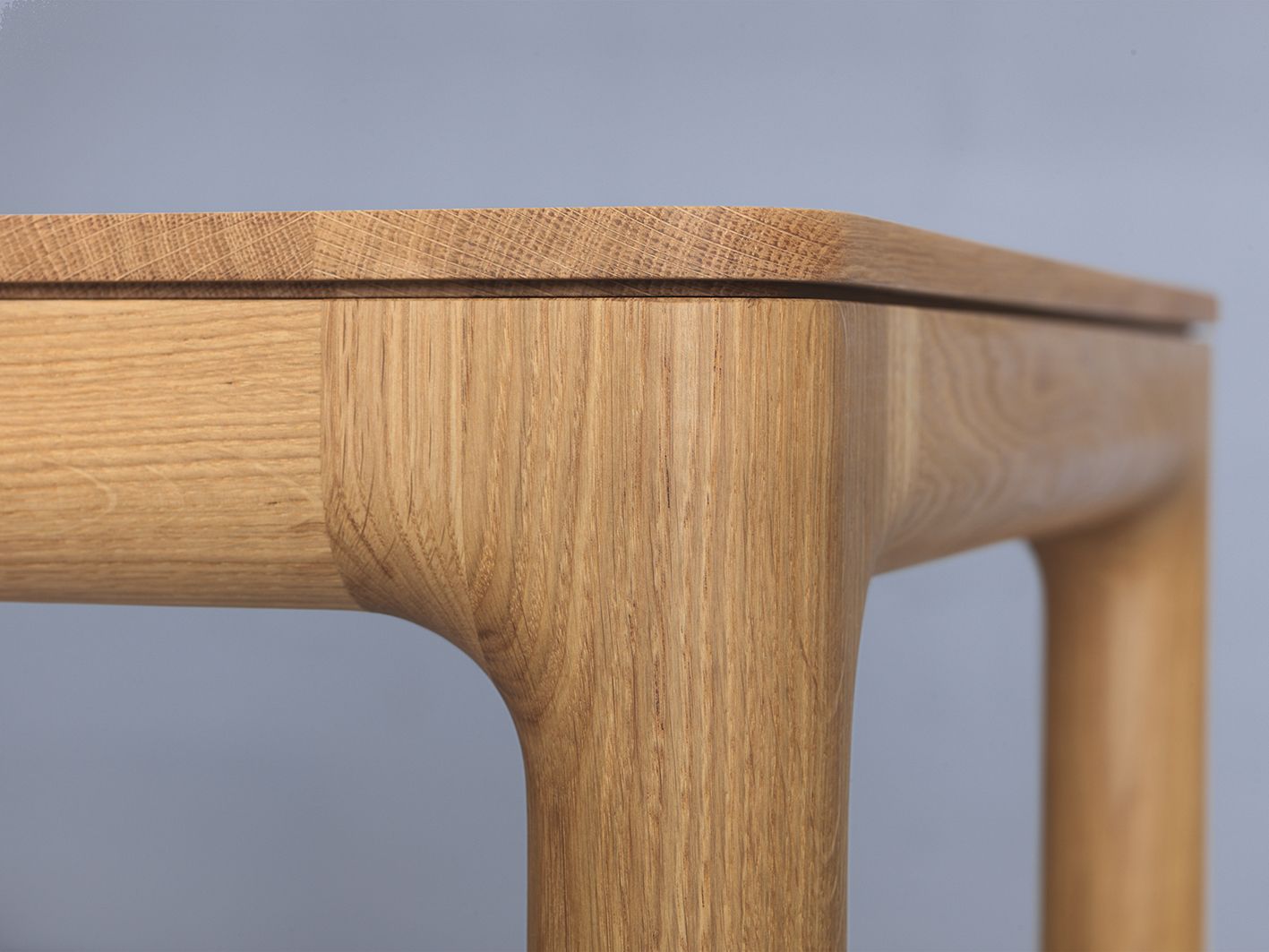 Detailaufnahme vom M11 Tisch: Massivholz Tischplatte und abgerundete Beine aus hellem Holz.