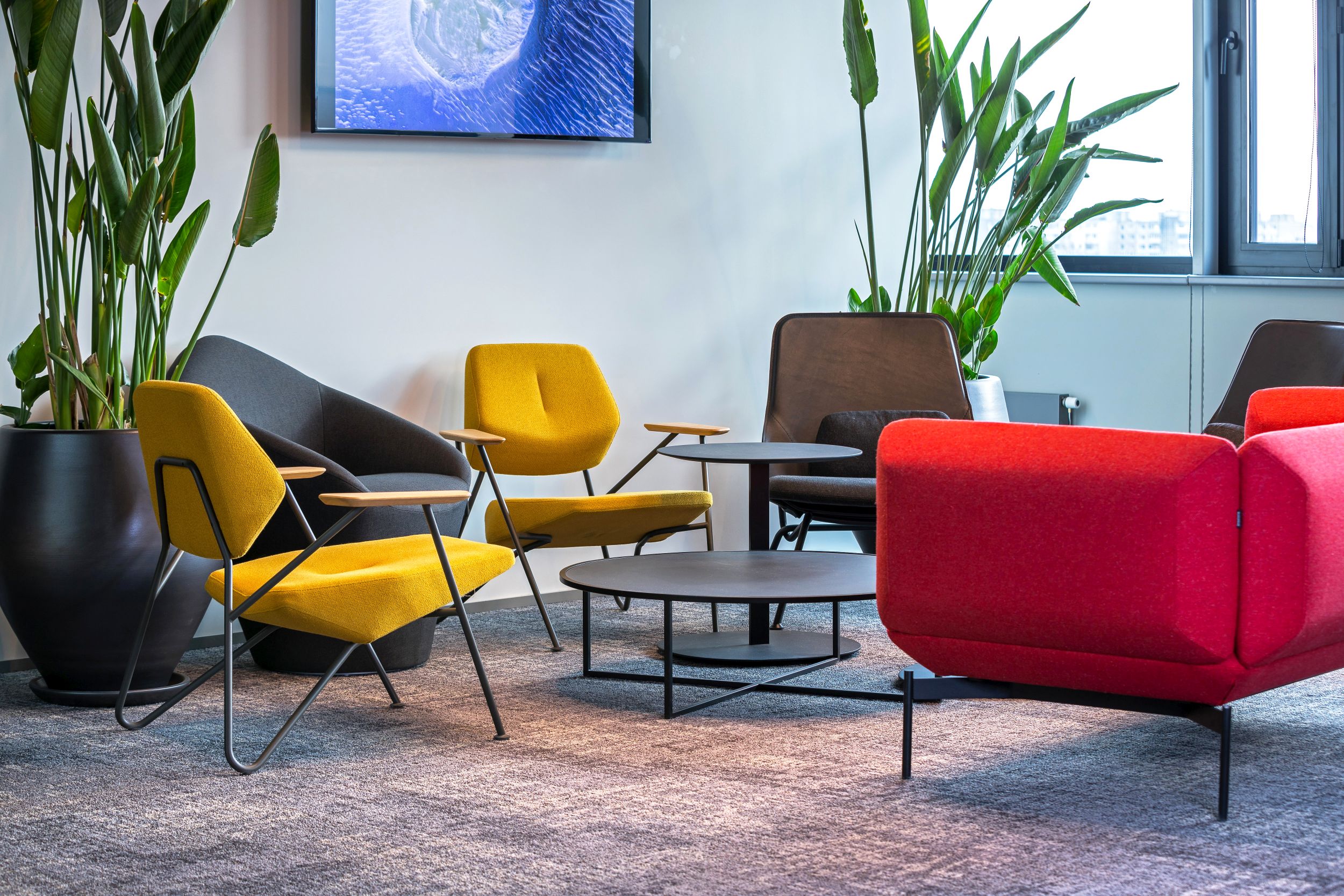 Innenaufnahme mit Prostoria Polygon Beistelltischen und farbenfrohen Sesseln in einem modernen Büro-Lounge-Bereich.