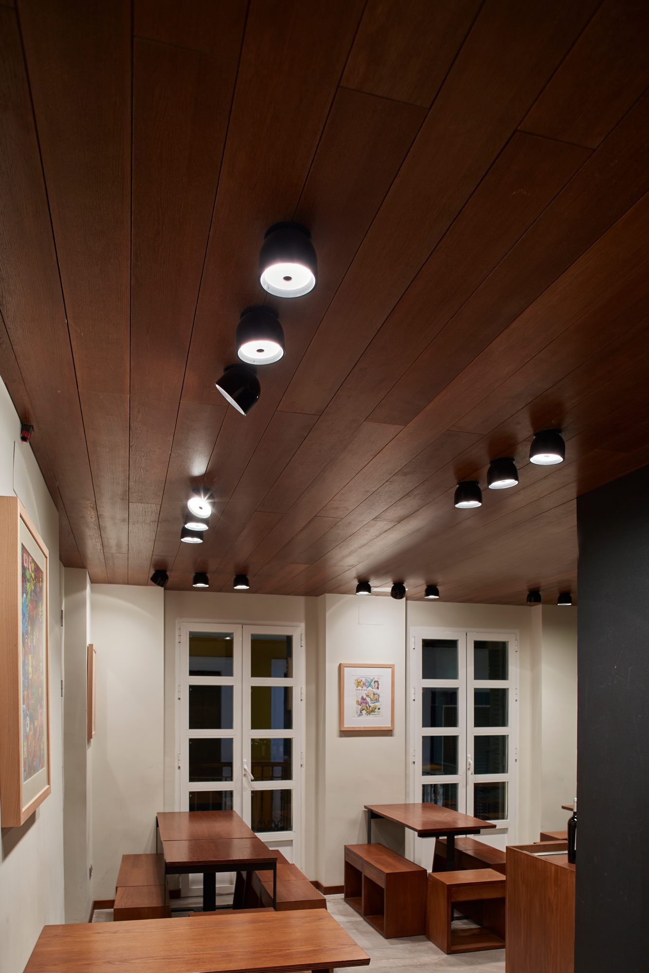 Innenaufnahme mit mehreren schwarzen Wan C/W Deckenleuchten von Flos an einer Holzdecke über Tischen.