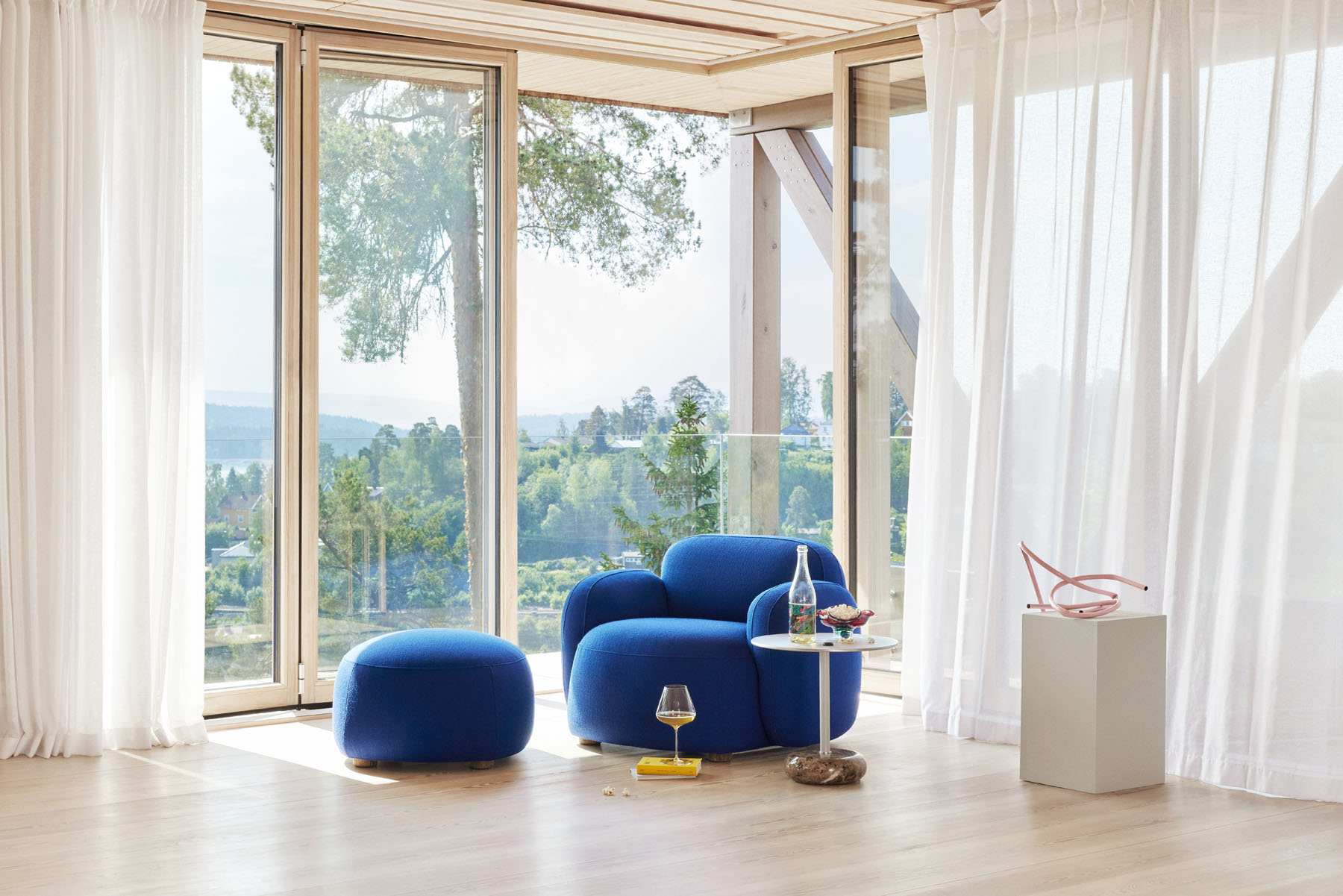 Gem Loungesessel mit Armlehne in Blau mit Hocker vor Fenster mit Ausblick.