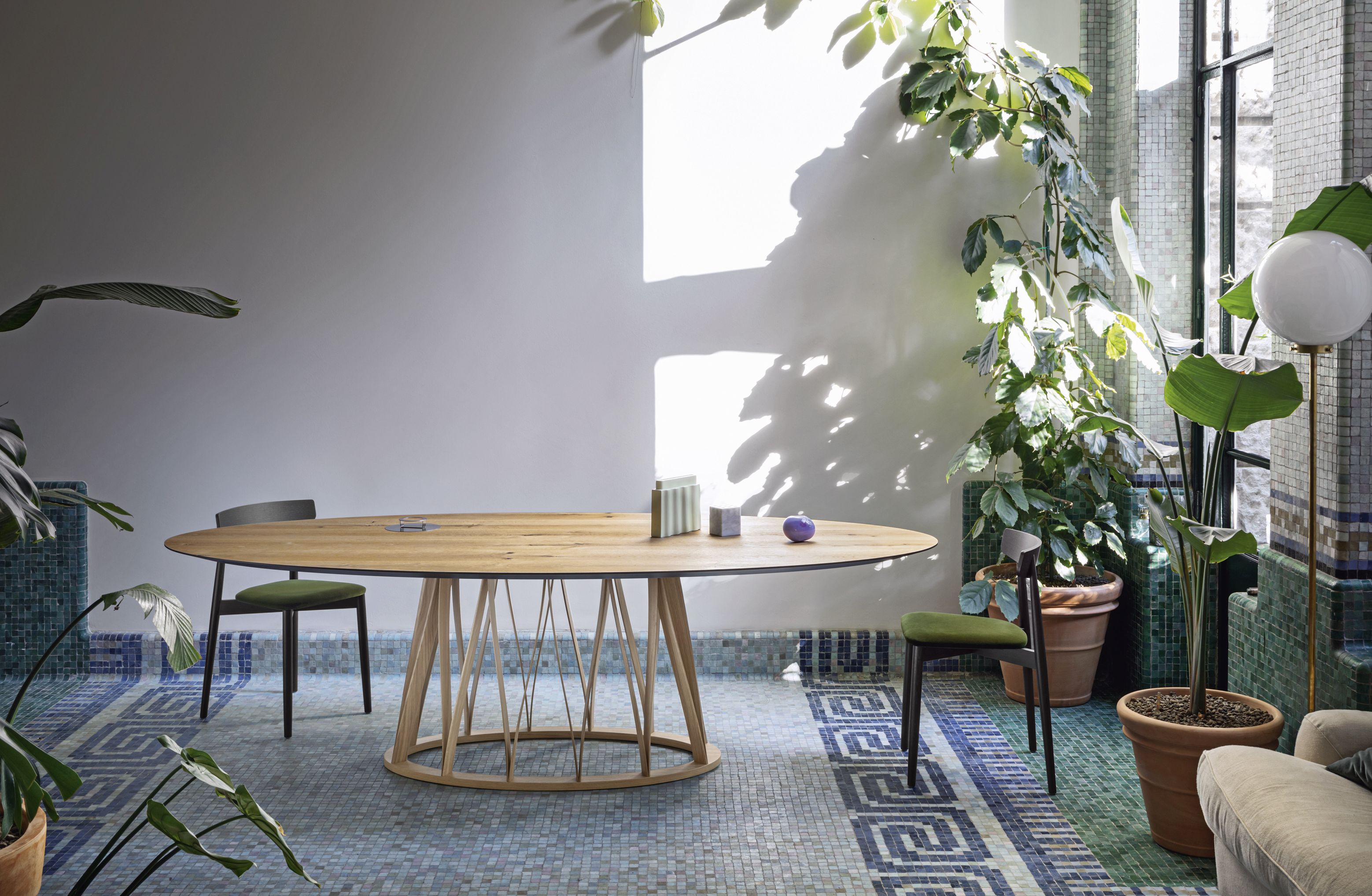 Acco Tisch Miniforms: Ovaler Holztisch mit filigranem Holzgestell in einem hellen, begrünten Raum.