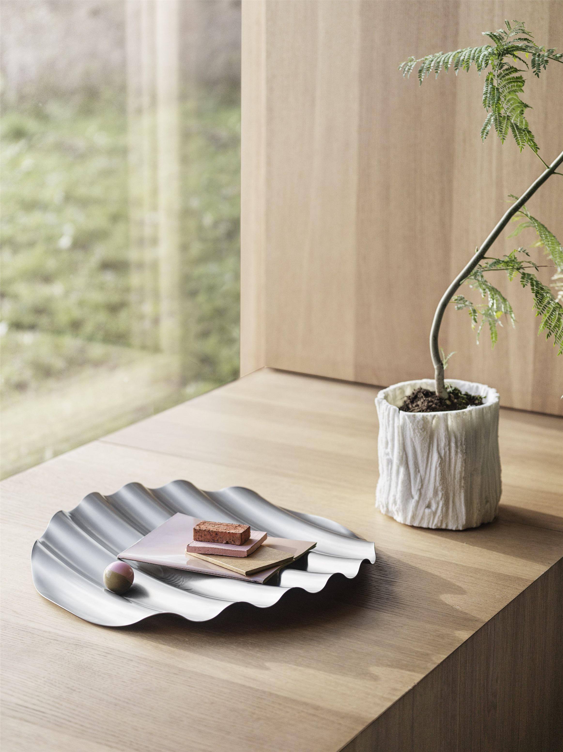 Muuto Wave Tray Schale aus Edelstahl auf Holztisch mit Dekoration und Zimmerpflanze.