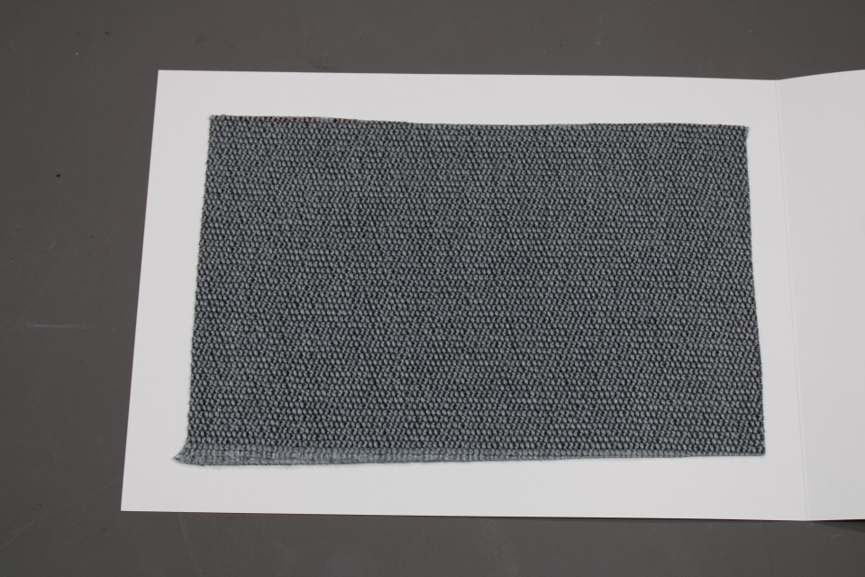 Stoffmusterkarte Gruppe 91 Cor: Nahaufnahme eines grauen, gewebten Stoffmusters auf weißem Karton.