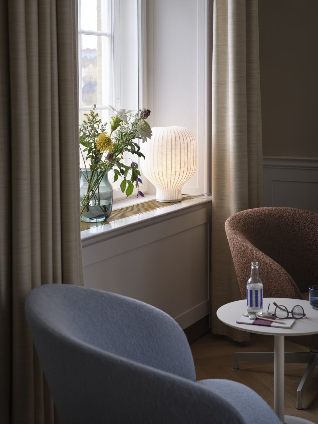 Weiße Muuto Strand Tischleuchte auf Fensterbank, neben Blumen und Vorhängen. Moderne Beleuchtung.