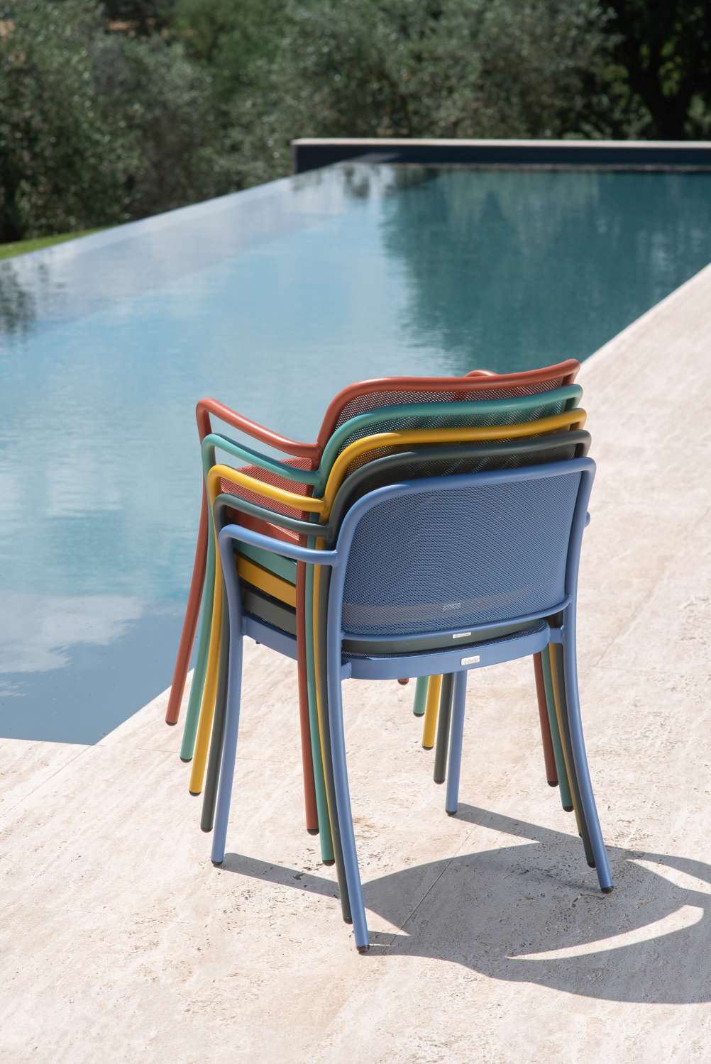 Gestapelte Emu Café Armchair Armlehnstühle in verschiedenen Farben für den Außenbereich am Pool.