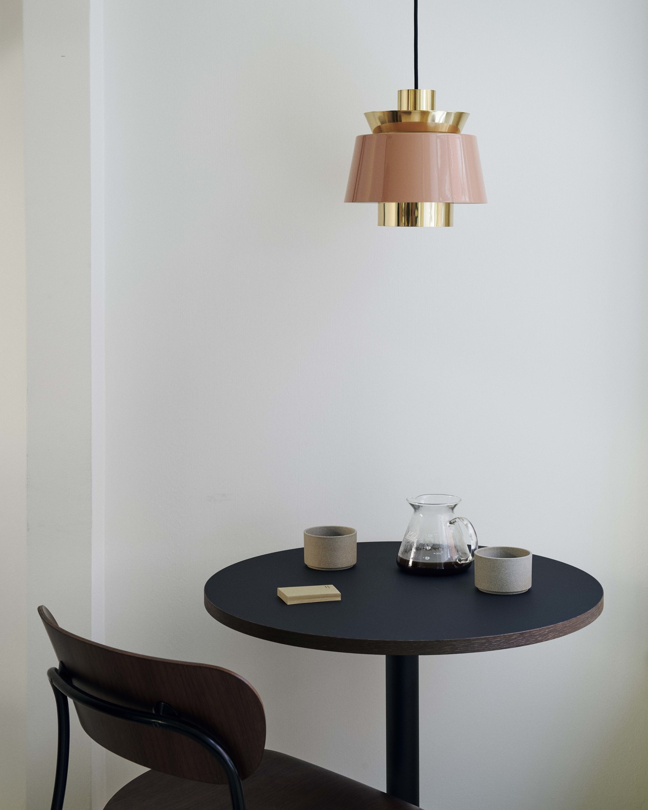 AndTradition Utzon JU1 Pendelleuchte in Rosa und Gold über einem Kaffeetisch mit Karaffe und Tassen.