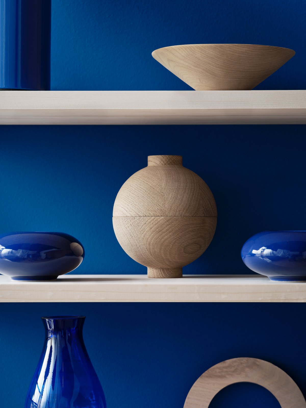 String Pocket Regal mit Holzschalen und blauen Vasen vor blauem Hintergrund. String Furniture.